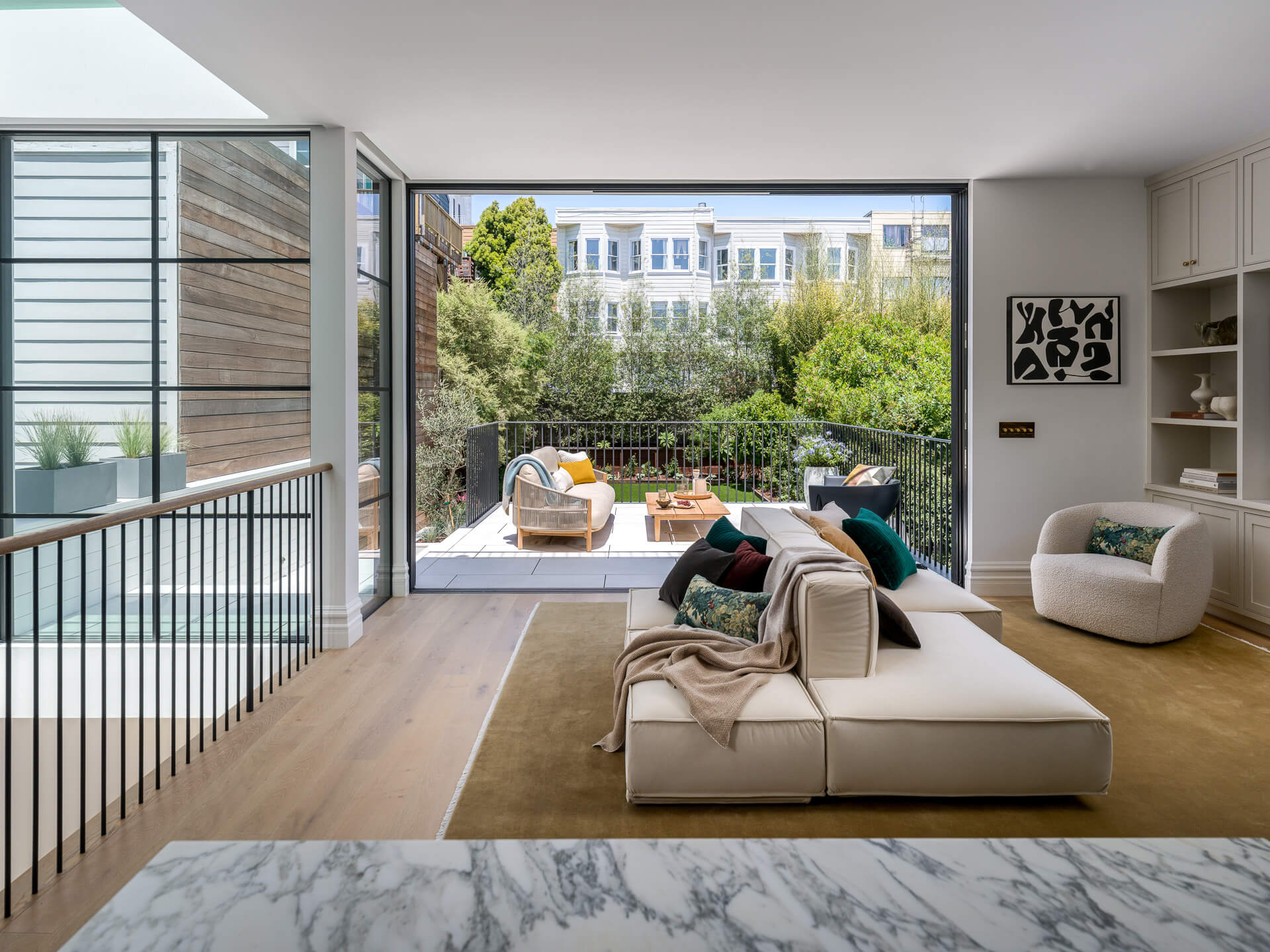 Contemporary living room with pale sectional, built-in shelving, and glass doors opening to a garden terrace.