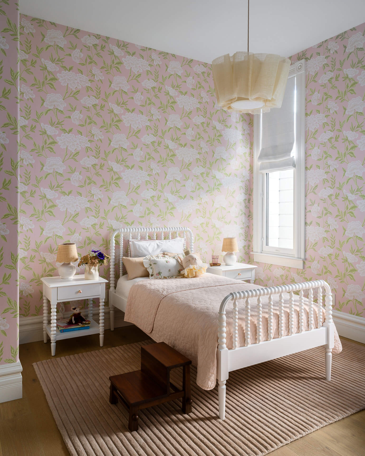 Child’s bedroom with botanical wallpaper, white spindle bed, striped rug, and matching nightstands.