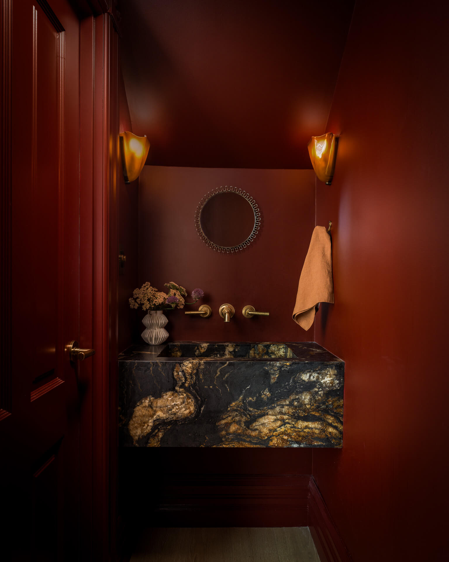 Deep red powder room with dramatically veined stone sink, brass fixtures, and warm wall sconces.