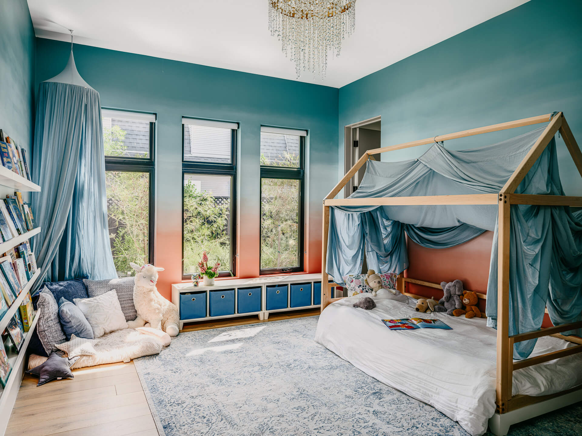 Teal children’s bedroom with canopy bed, window bench, bookshelves, and soft blue furnishings.