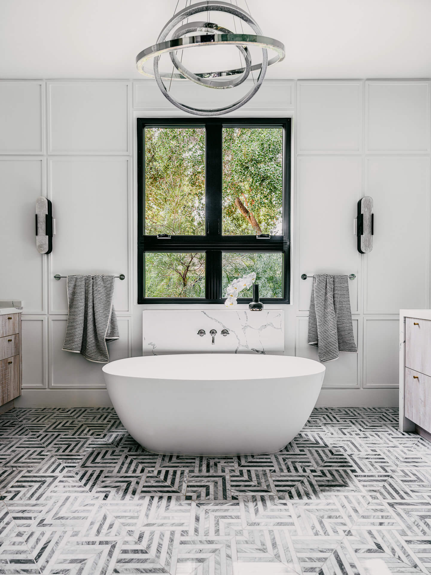 Bright bathroom with freestanding white tub, graphic black-and-white tile floor, and black-framed window.