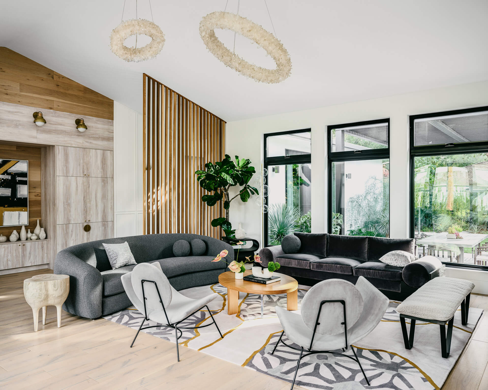 Contemporary living room with curved gray seating, wood-slat partition, woven pendant lights, and garden views.