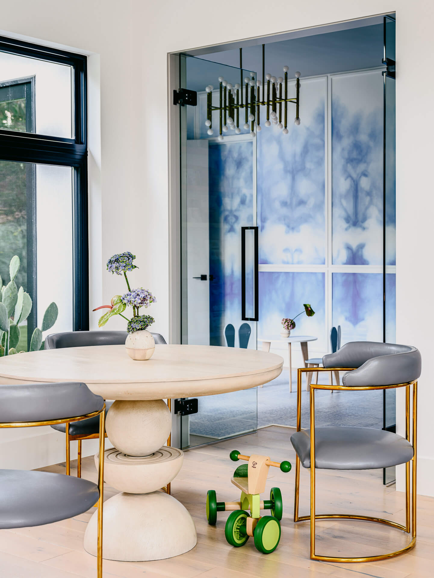 Breakfast nook with round stone table, gray chairs, black-framed window, and blue glass door.