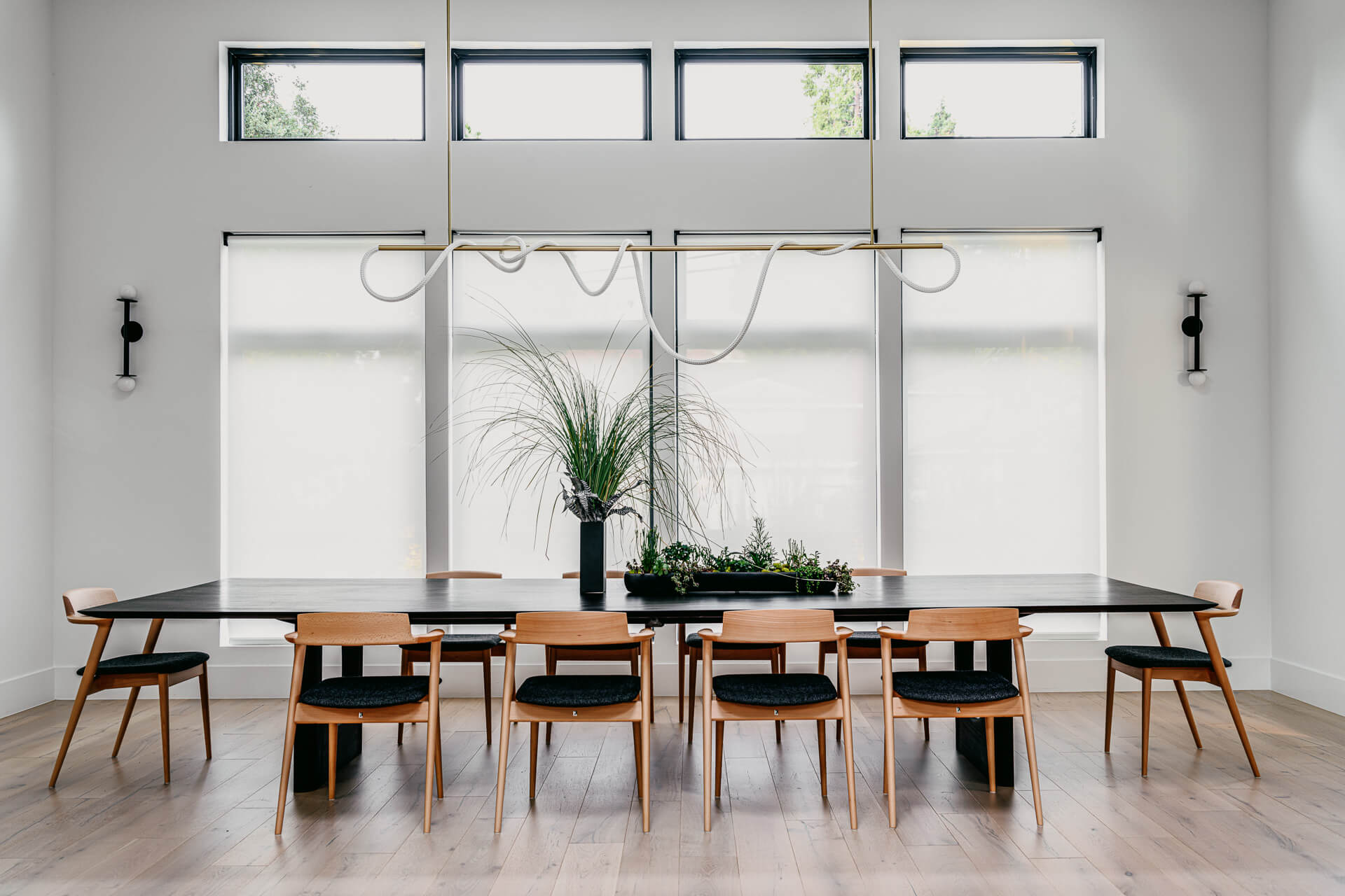 Minimal dining room with long wood table, black-and-wood chairs, and a sculptural linear chandelier.