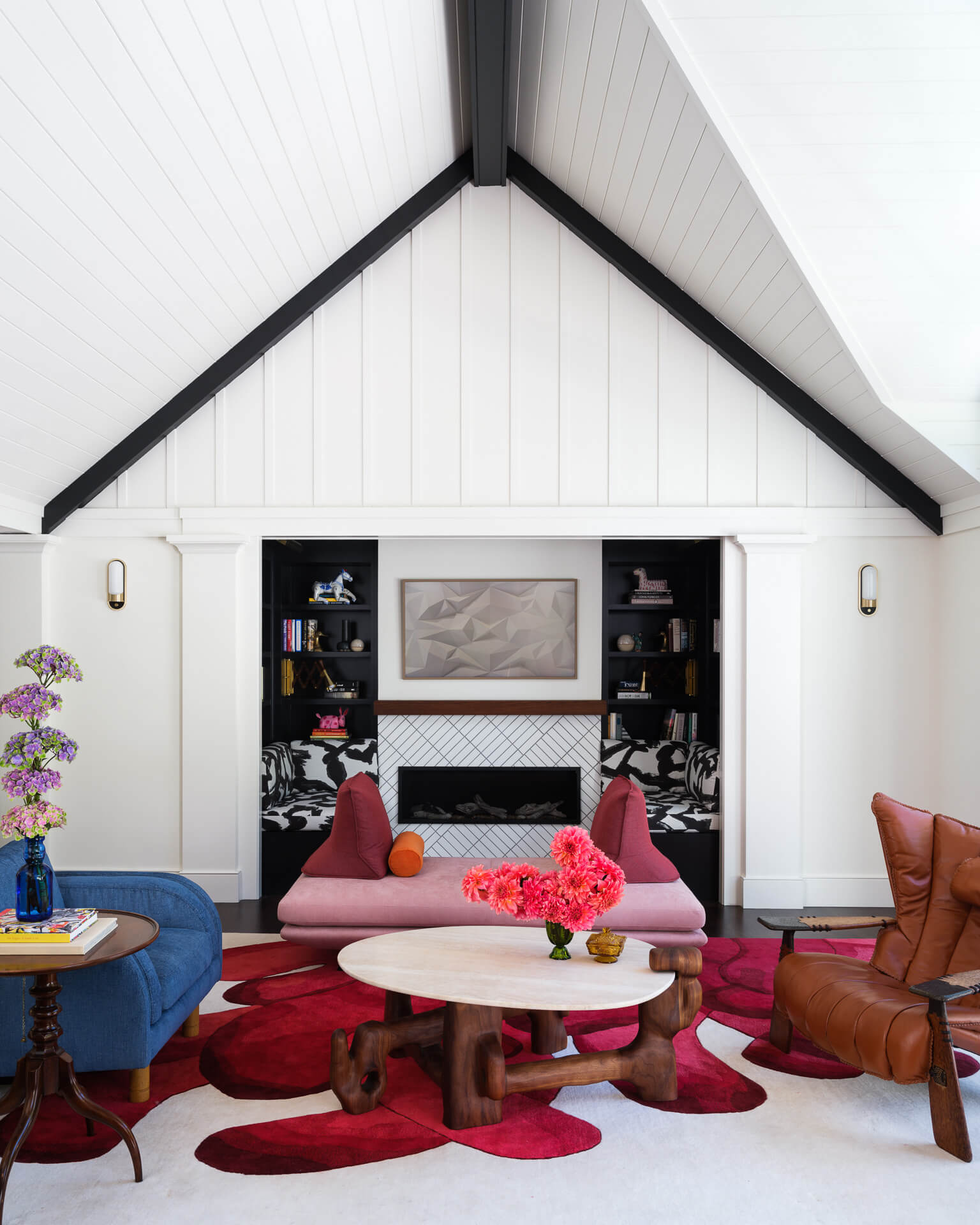 Vaulted living room with white fireplace, colorful seating, sculptural coffee table, and bold red rug.
