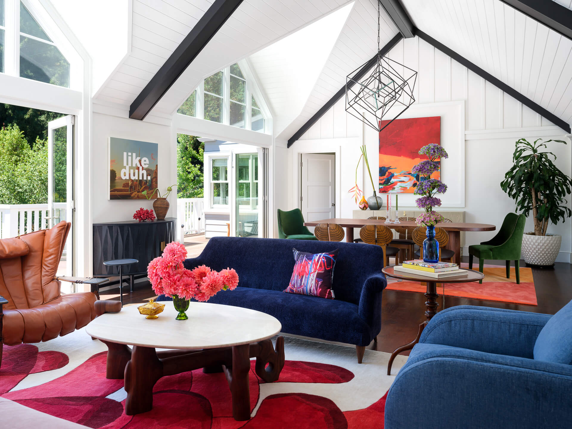 Bright open living and dining room with blue velvet seating, colorful artwork, and vaulted ceiling.