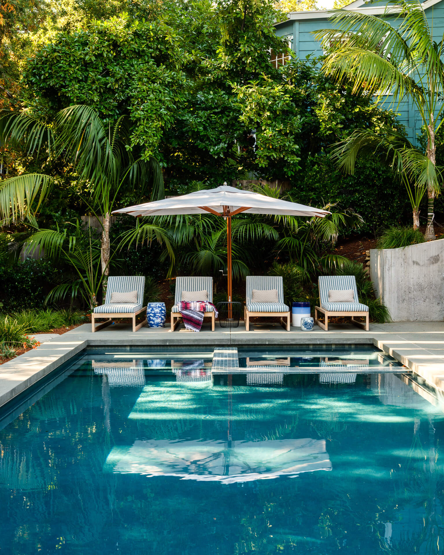 Turquoise swimming pool with shaded lounge chairs and dense tropical greenery.