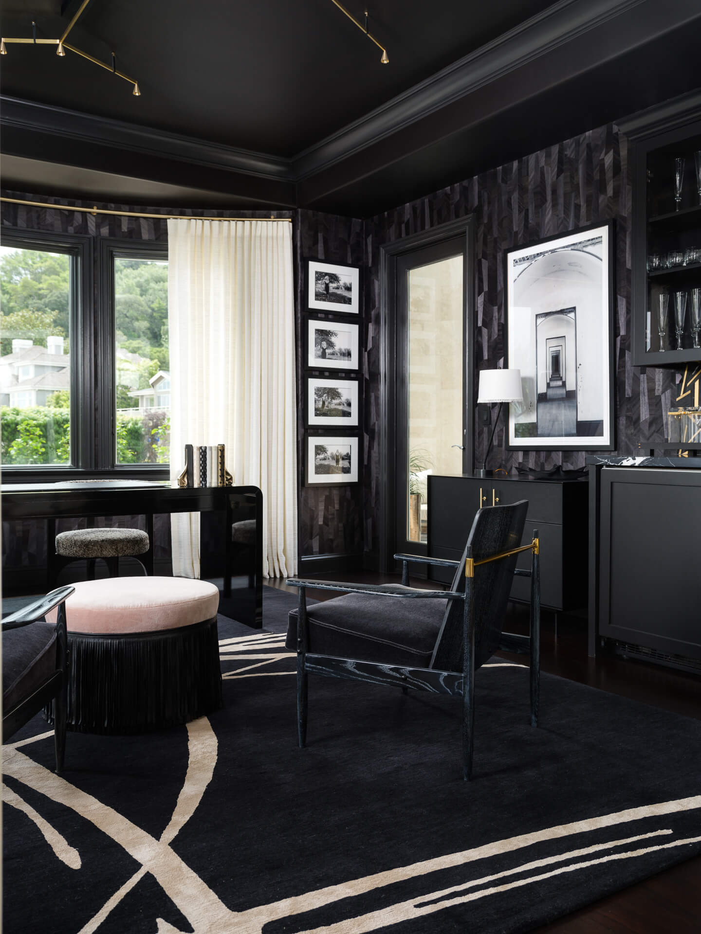 Moody black home office with dark wood cabinetry, lounge chair, graphic rug, and framed black-and-white artwork.