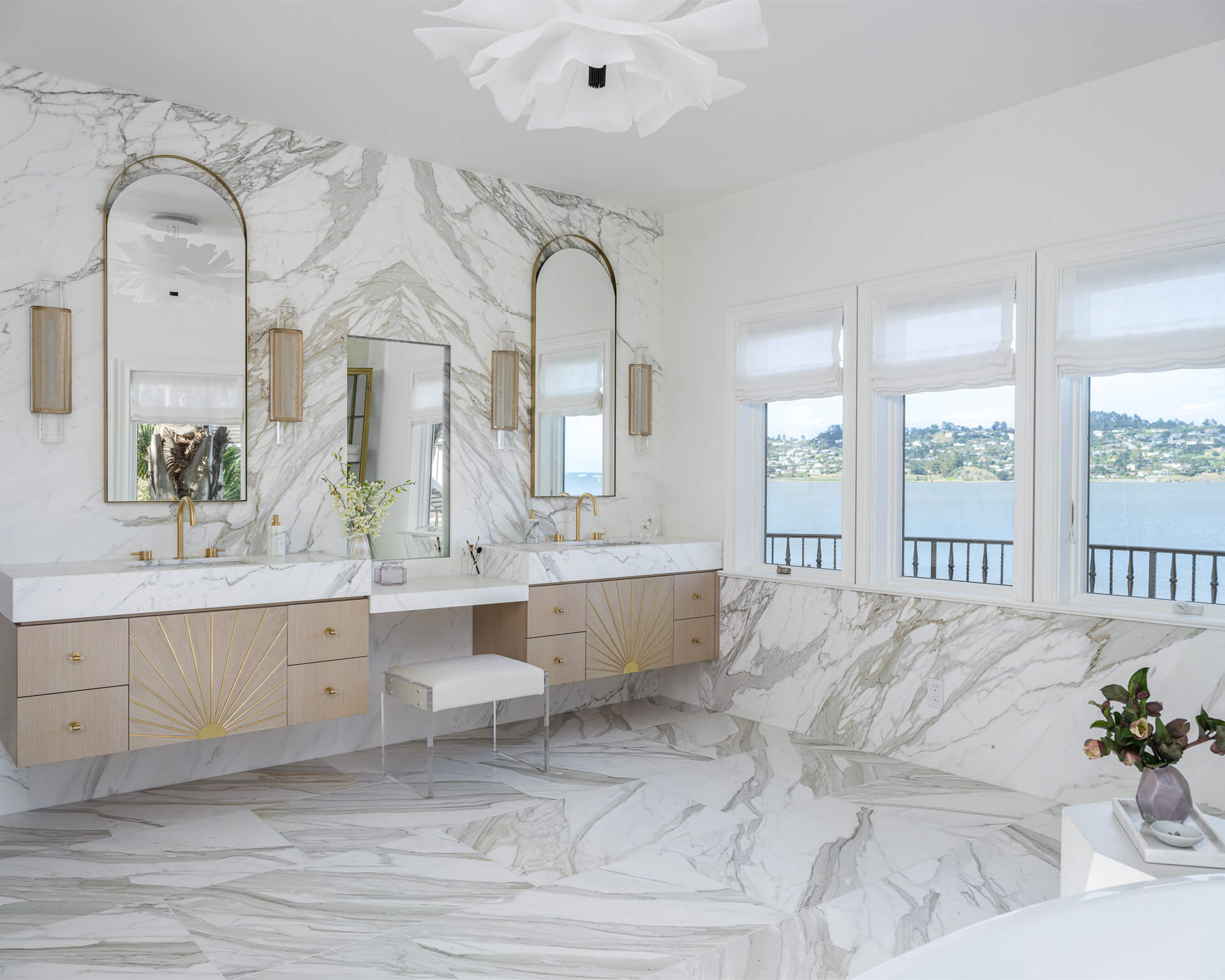 Spacious white marble bathroom with long double vanity, arched mirrors, and windows overlooking the water.