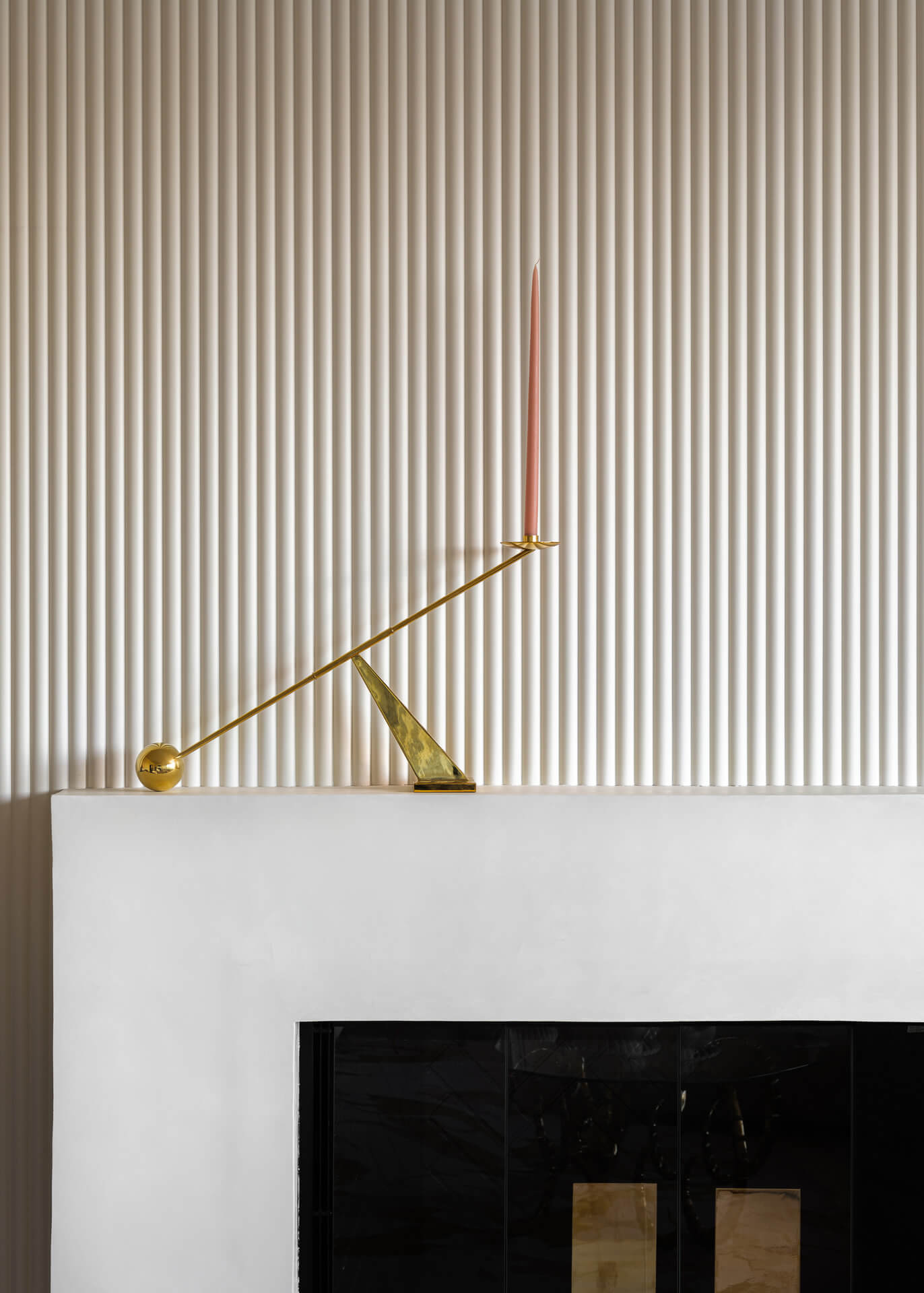 Minimal fireplace with vertically ribbed wall treatment and a slender brass sculpture on the mantel.