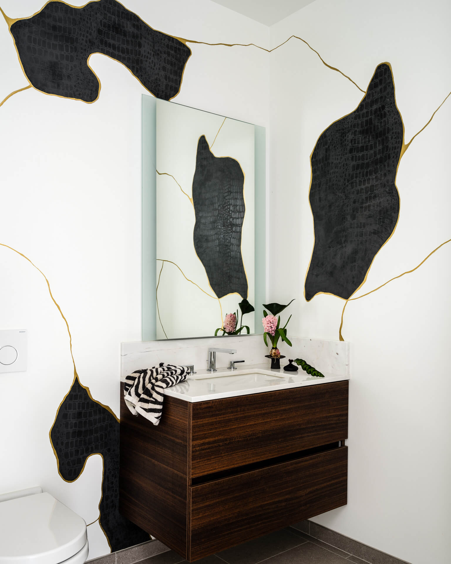 Powder room with bold black leaf-patterned walls, floating wood vanity, tall mirror, and brass fixtures.
