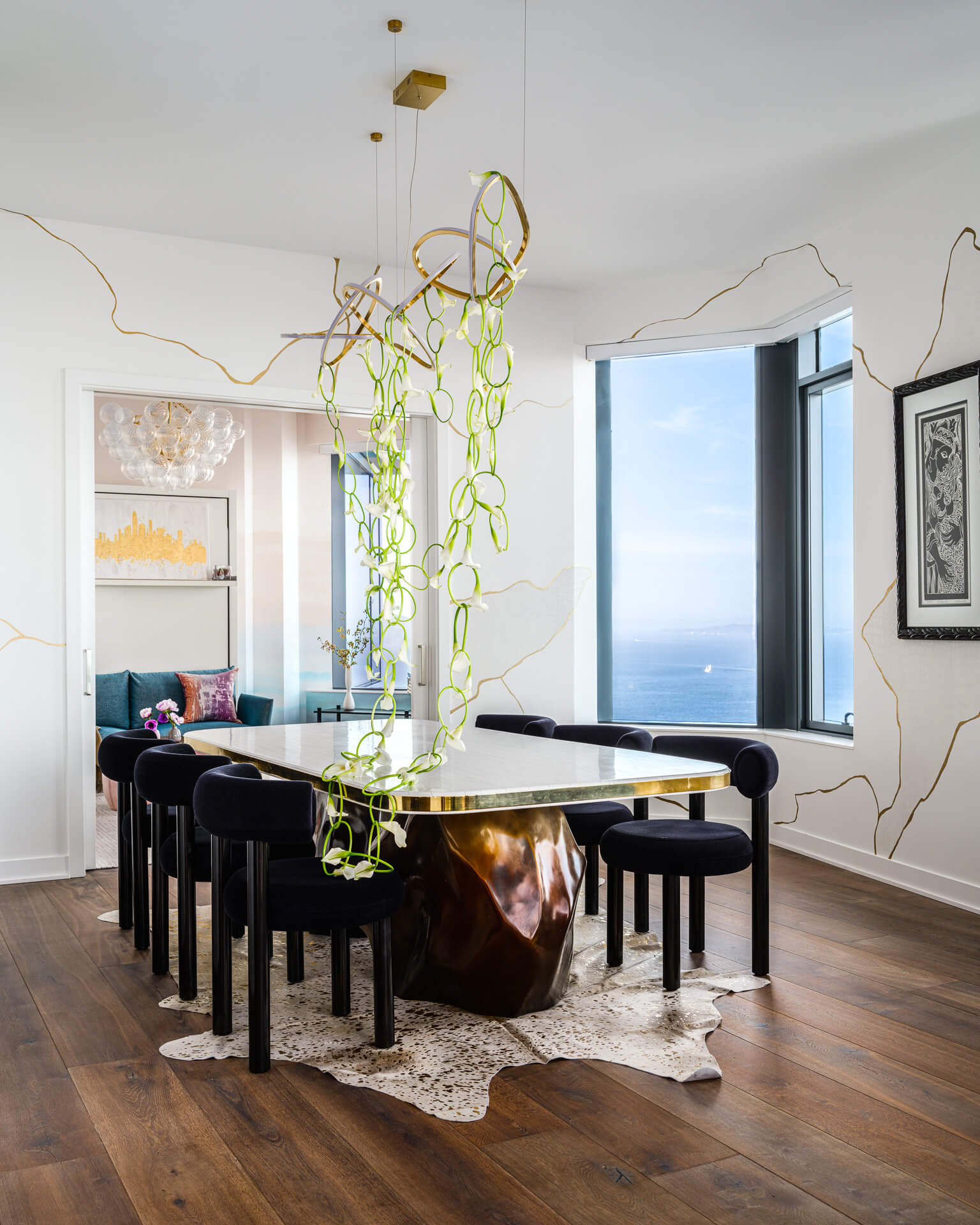 Dining room with reflective table, black chairs, hanging glass sculpture, and floor-to-ceiling windows overlooking the bay.