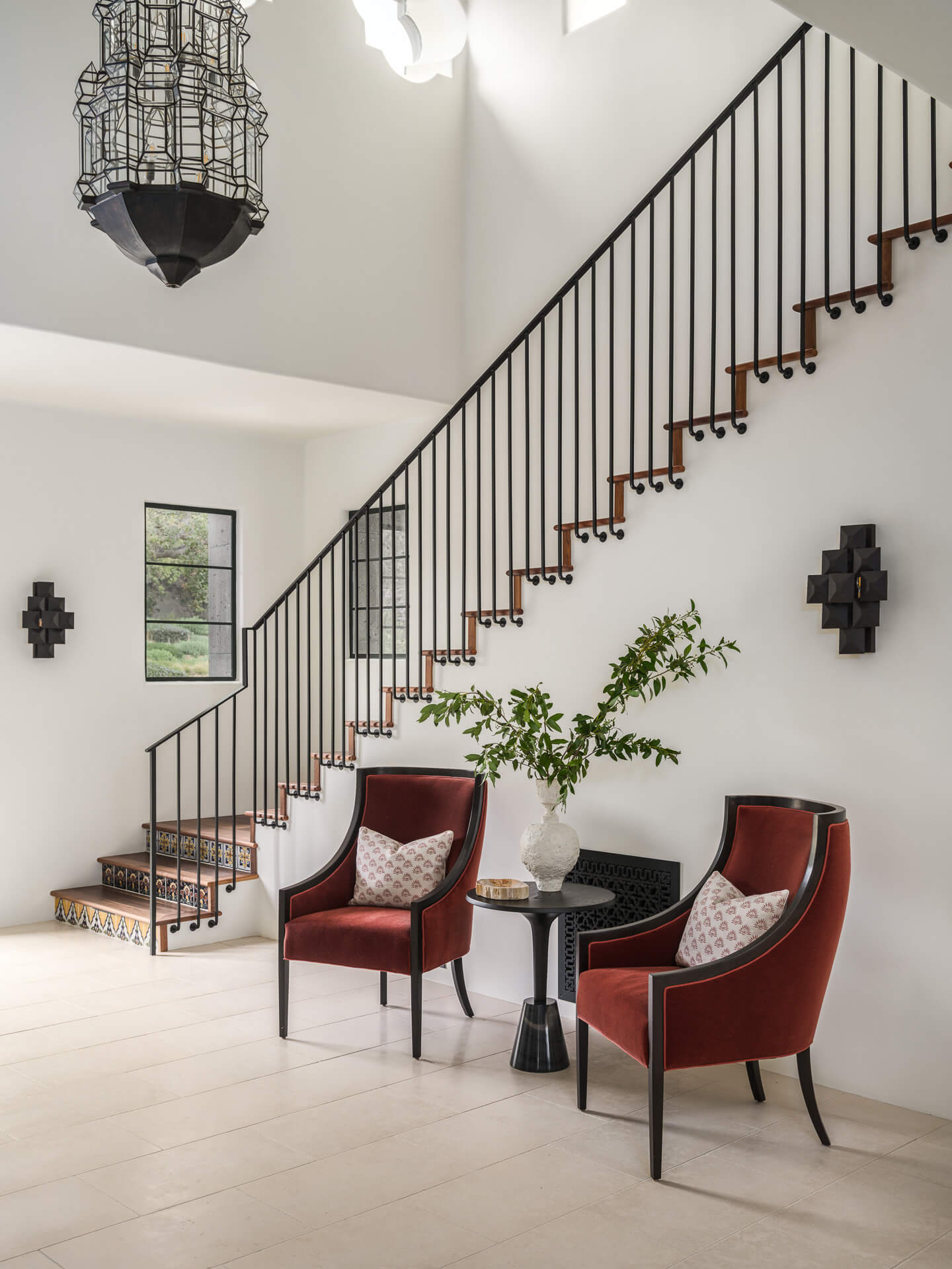 Bright entry with black metal staircase, two rust-colored chairs, small round table, and hanging lantern.