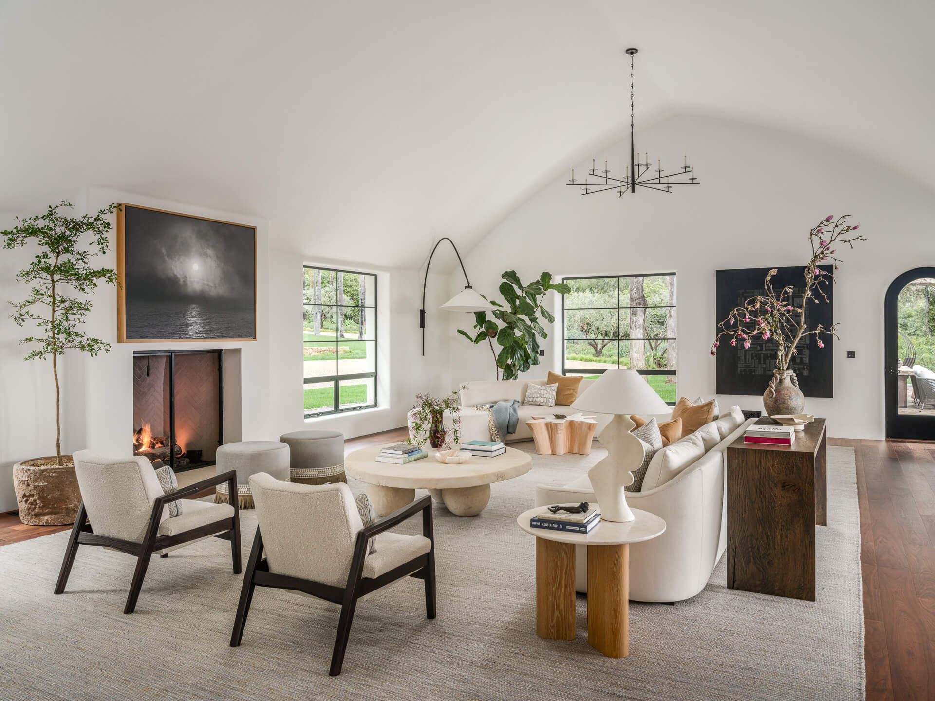 Airy living room with neutral seating, fireplace, vaulted ceiling, and black-framed windows overlooking the garden.