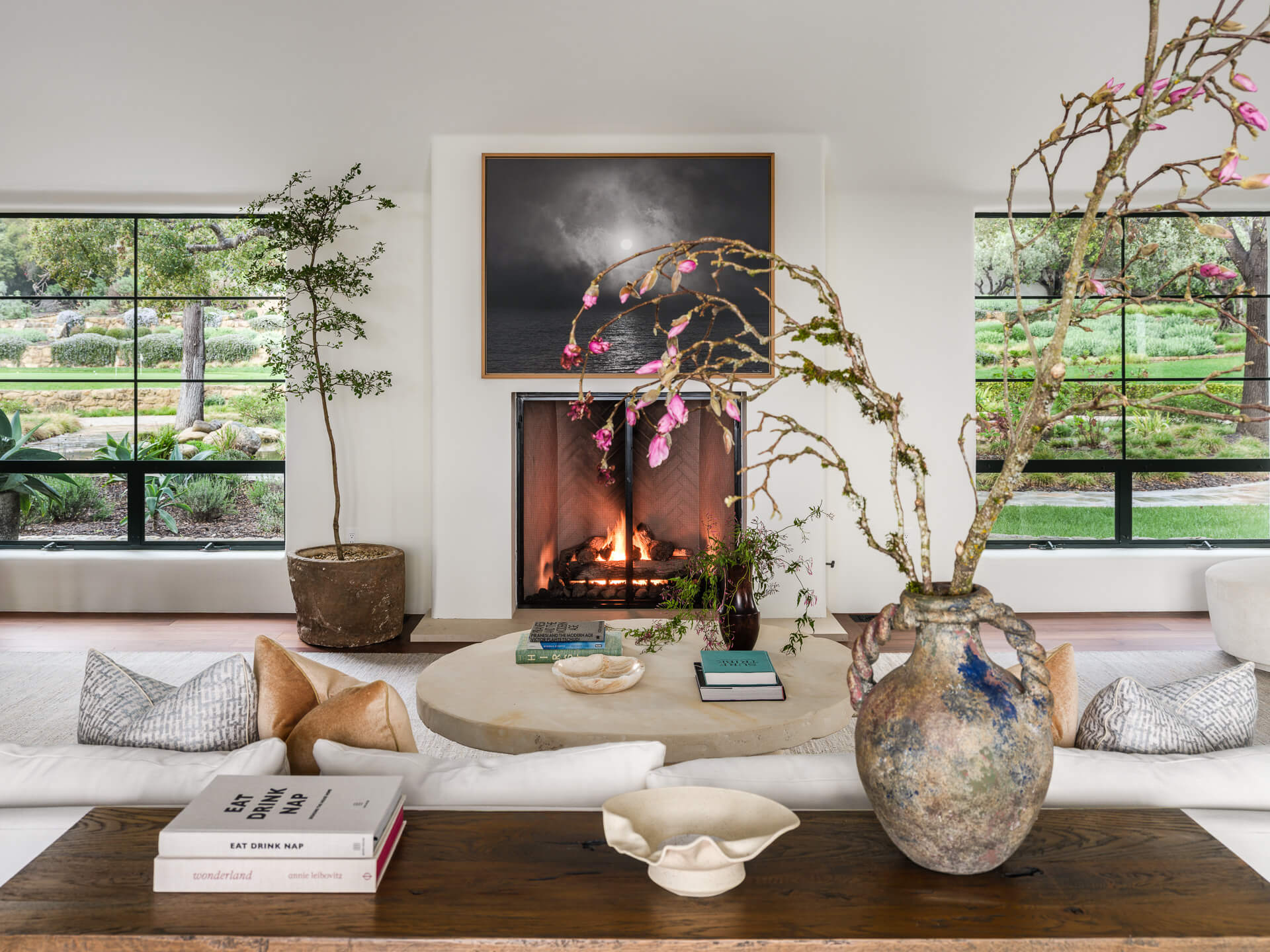 Living room detail with built-in window seating, fireplace, flowering branches, and layered decorative objects.