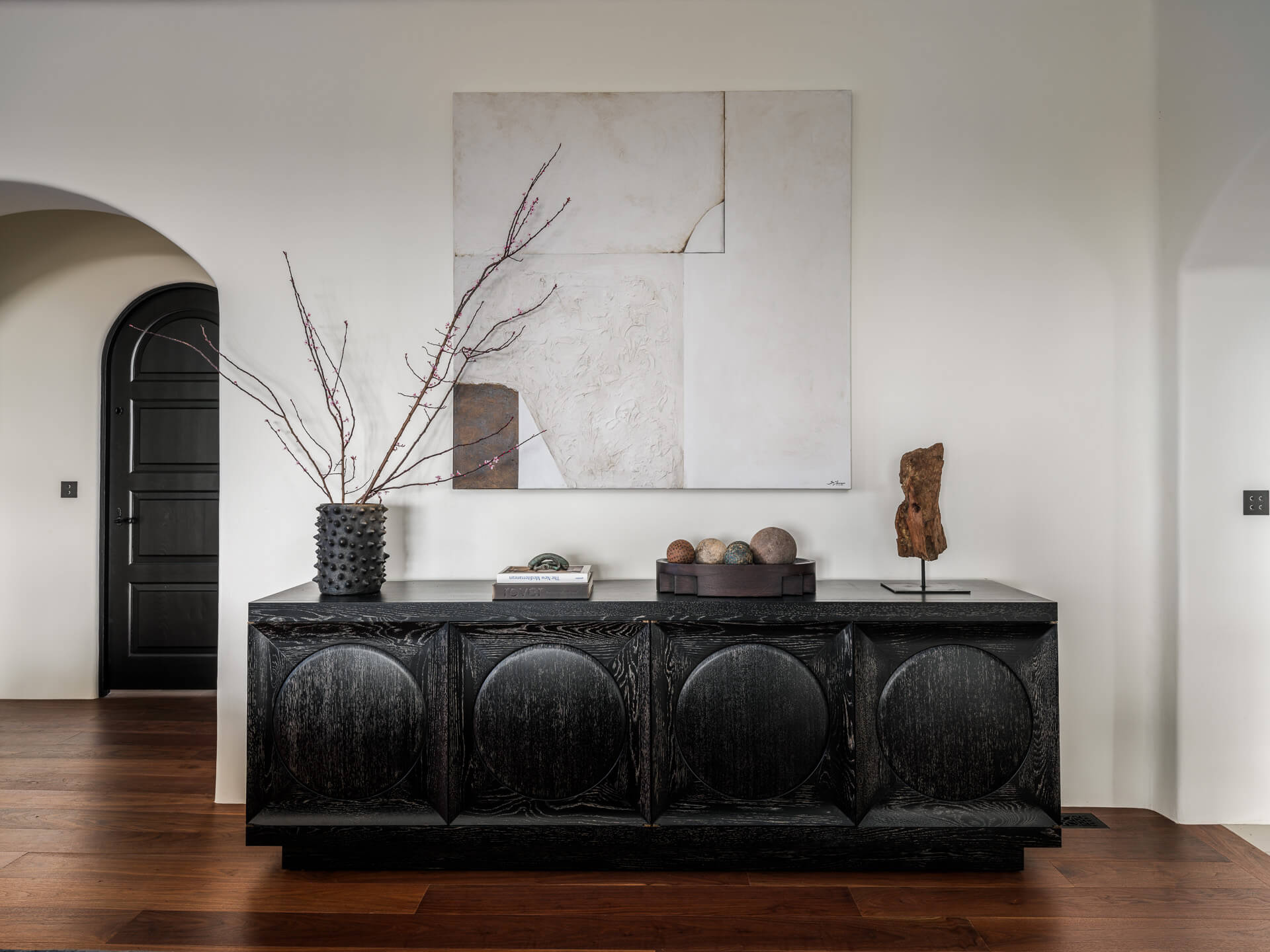 Black carved console beneath abstract artwork, styled with branches and sculptural objects.
