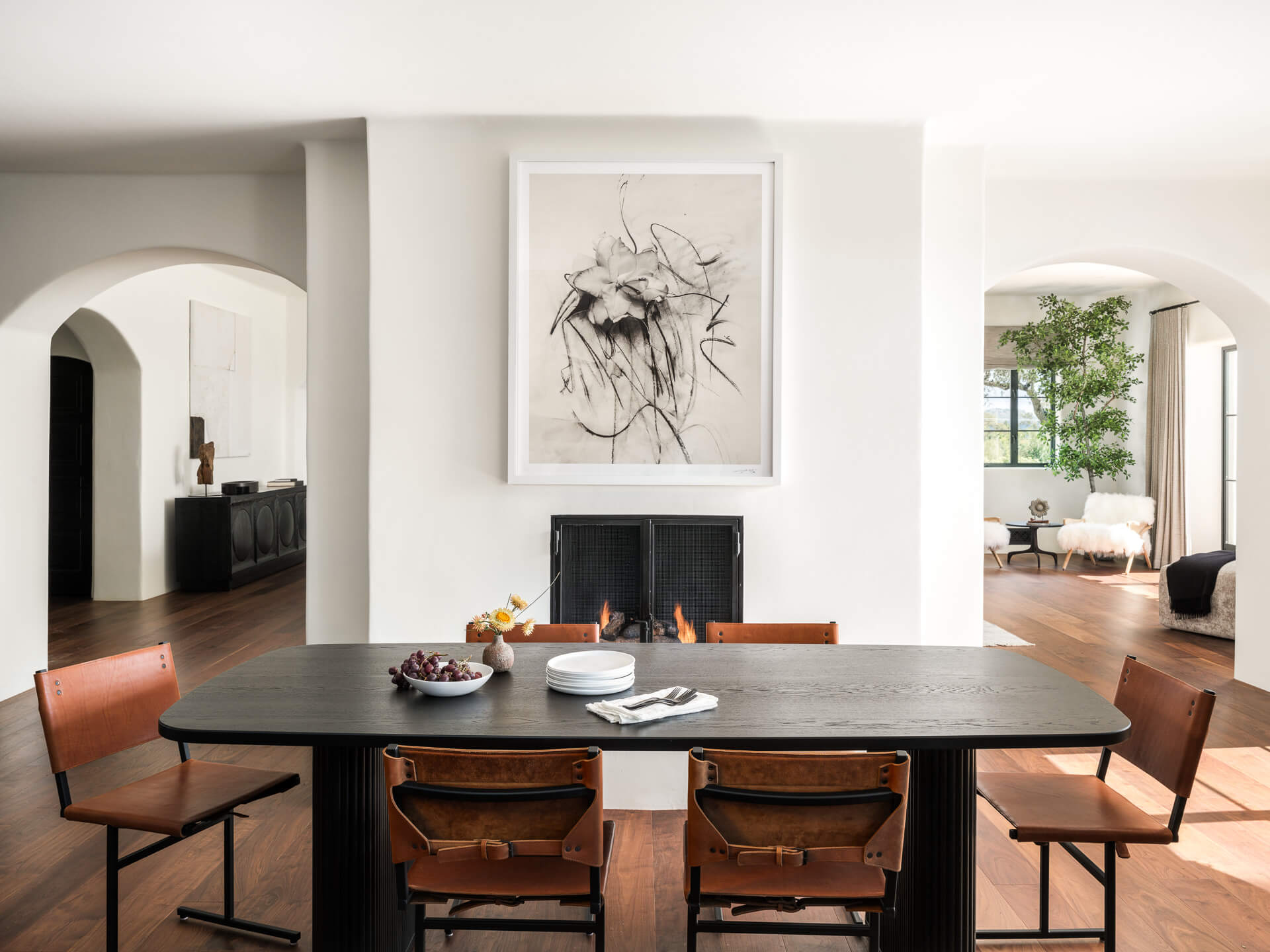 Dining area with dark rectangular table, leather chairs, fireplace, and abstract artwork.
