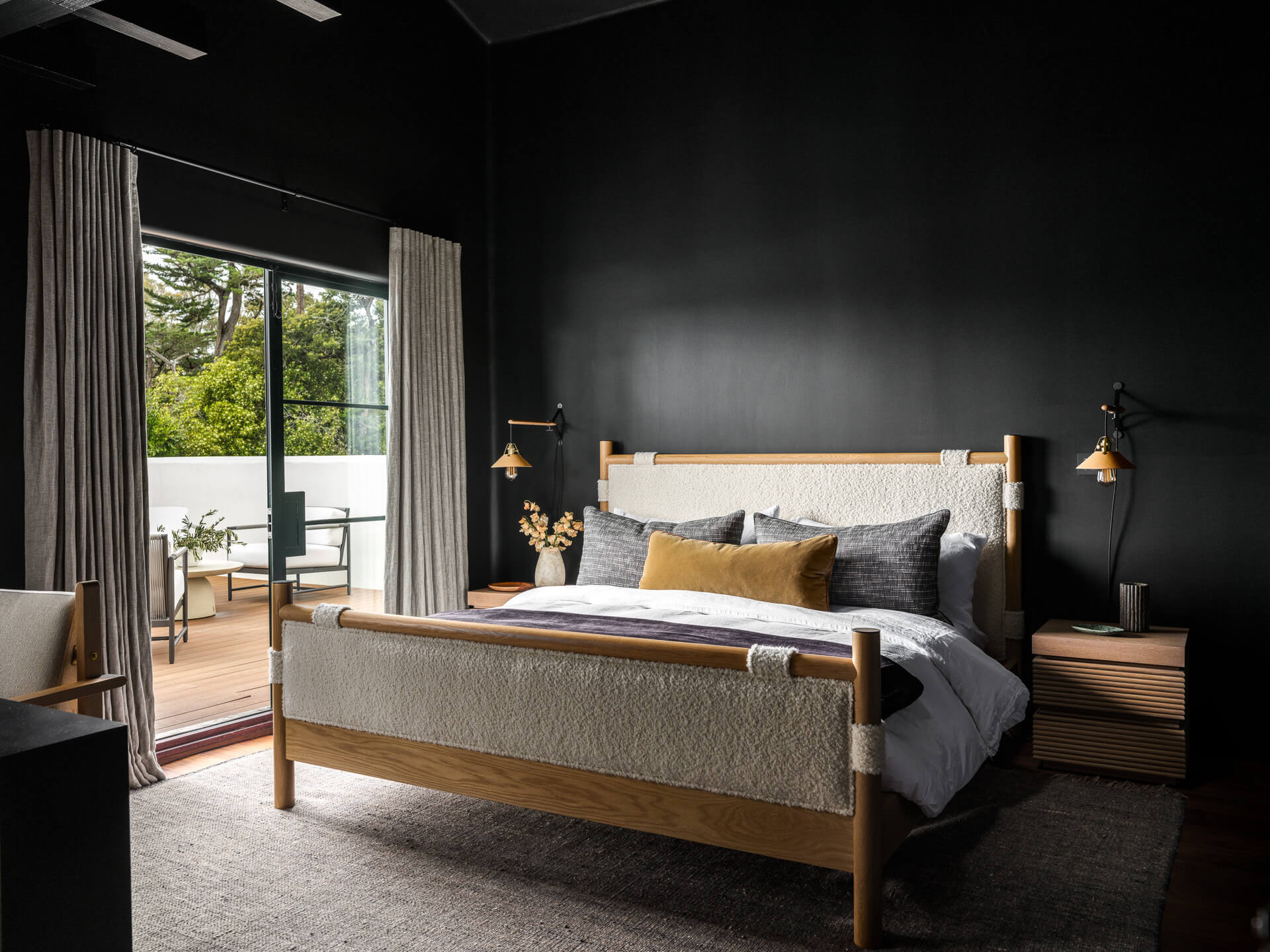 Moody bedroom with dark walls, wood bed, neutral bedding, and glass doors opening to a terrace.