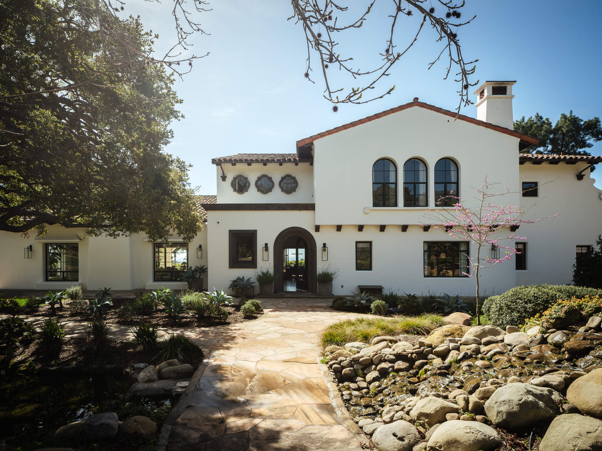 White Spanish-style home with arched windows, red tile roof, and landscaped stone garden.