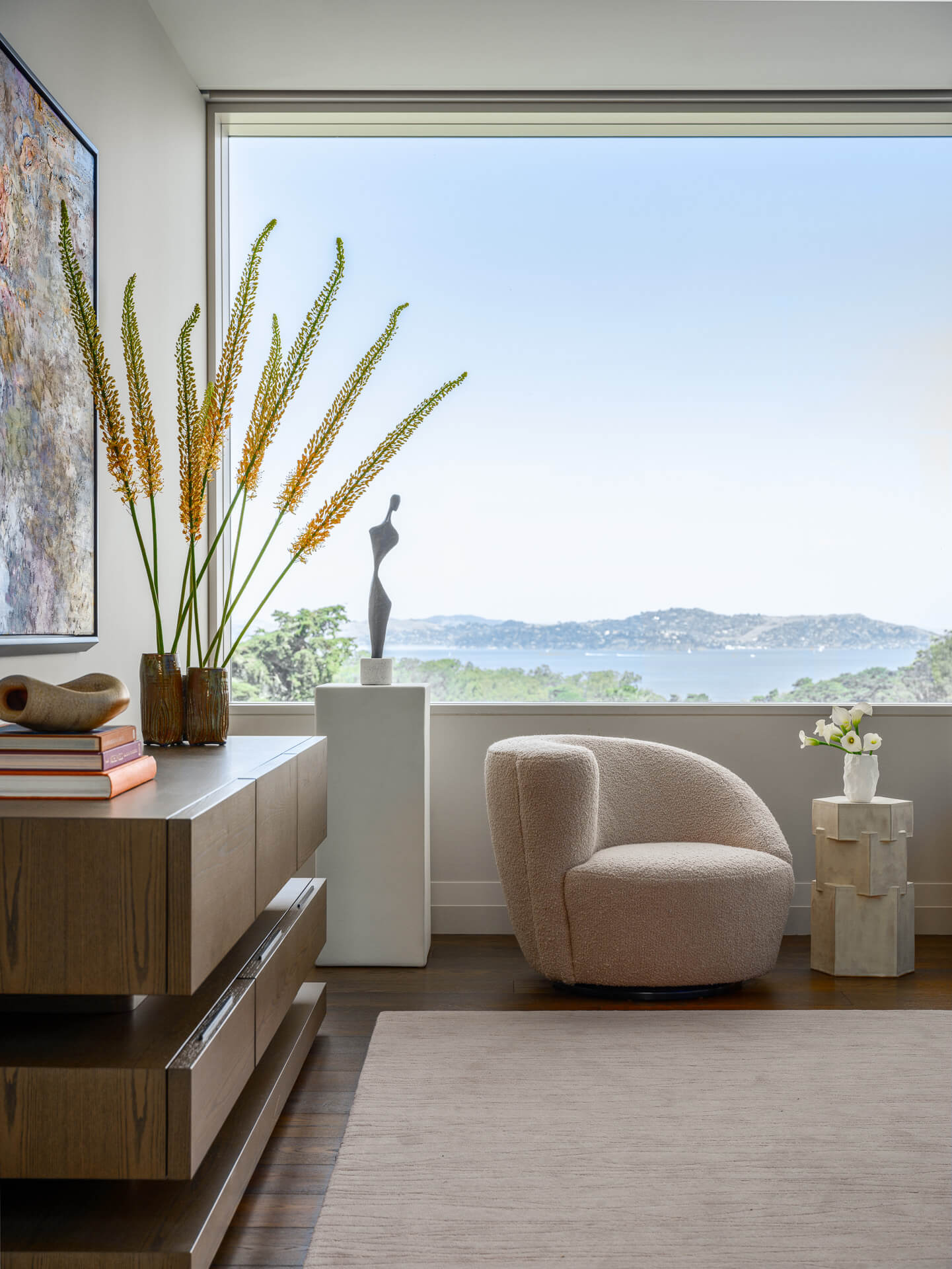 Bedroom sitting area with low wood dresser, rounded chair, and expansive views of the hills and bay.