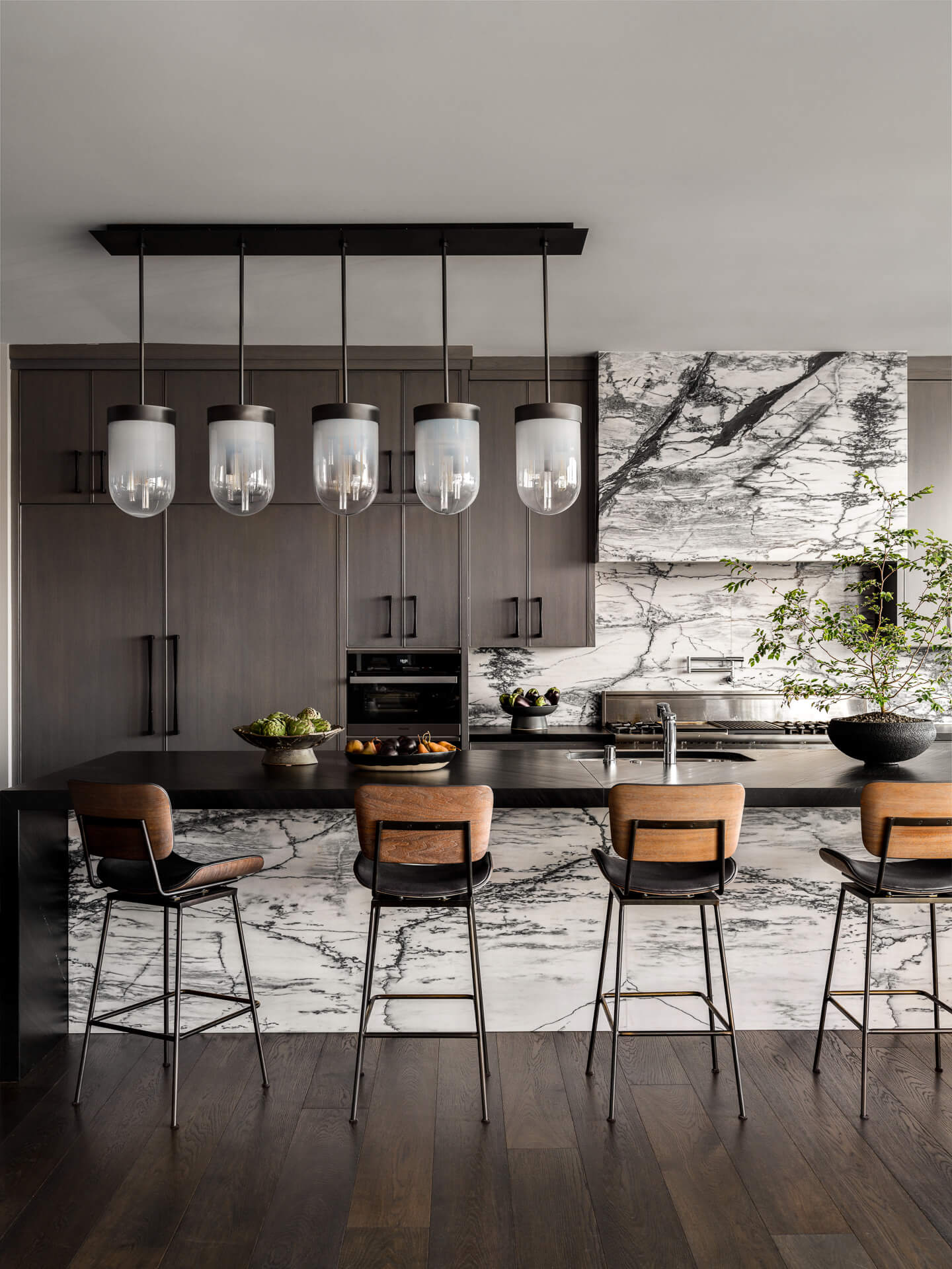 Modern kitchen with dark wood cabinetry, dramatic marble surfaces, pendant lights, and counter seating.