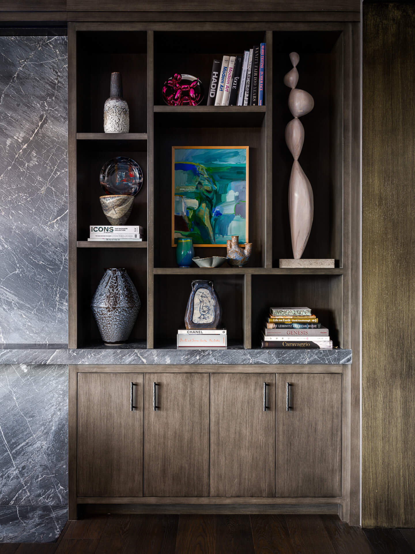 Dark wood built-in shelving displaying books, ceramics, artwork, and sculptural objects.