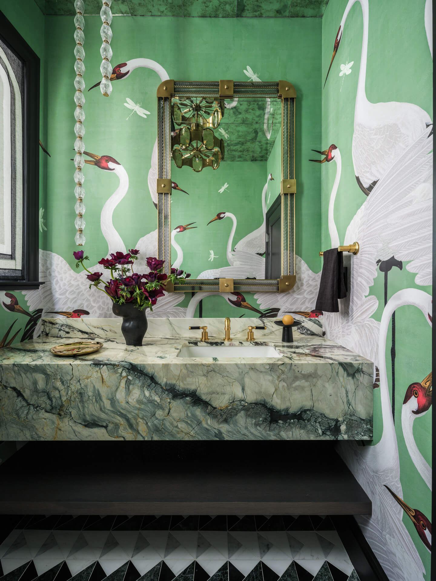 Powder room with green swan wallpaper, dramatically veined stone vanity, ornate mirror, and brass fixtures.