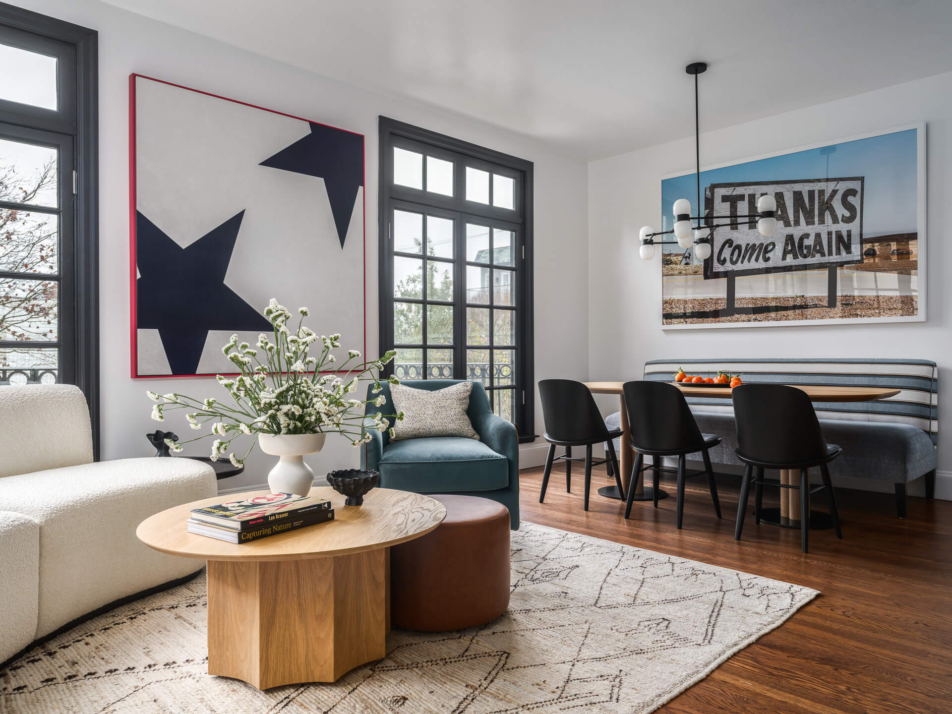 Bright living and dining area with white sofa, round wood coffee table, black chairs, and bold contemporary artwork.