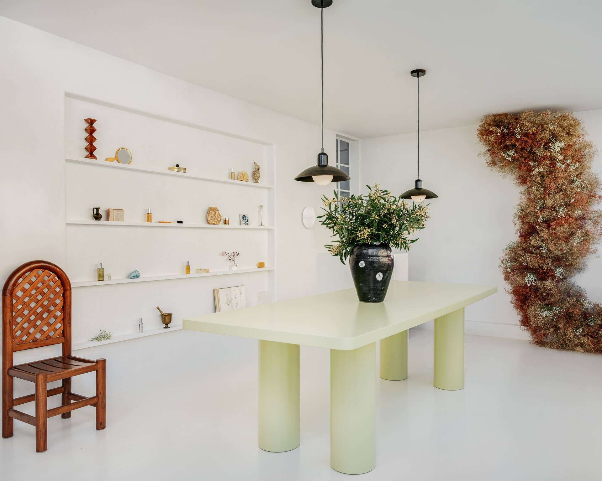 Minimal white spa interior with pale green table, black pendant lights, built-in display shelves, and dried floral installation.
