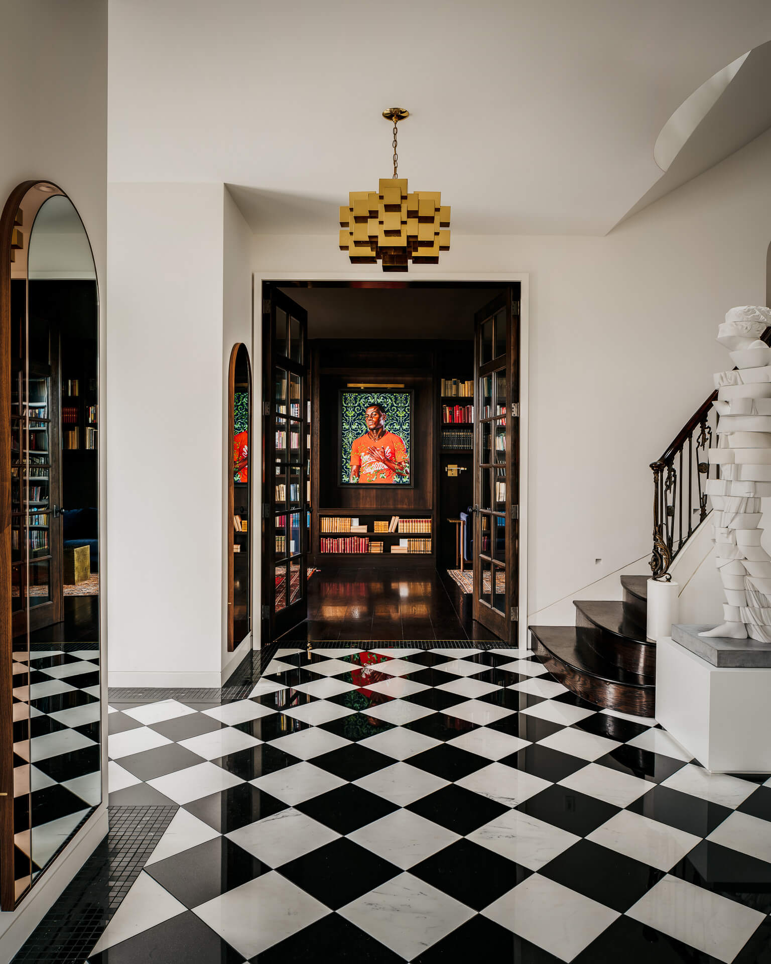 Entry hall with black-and-white checkerboard floor leading to a dark wood doorway framed by bookshelves.