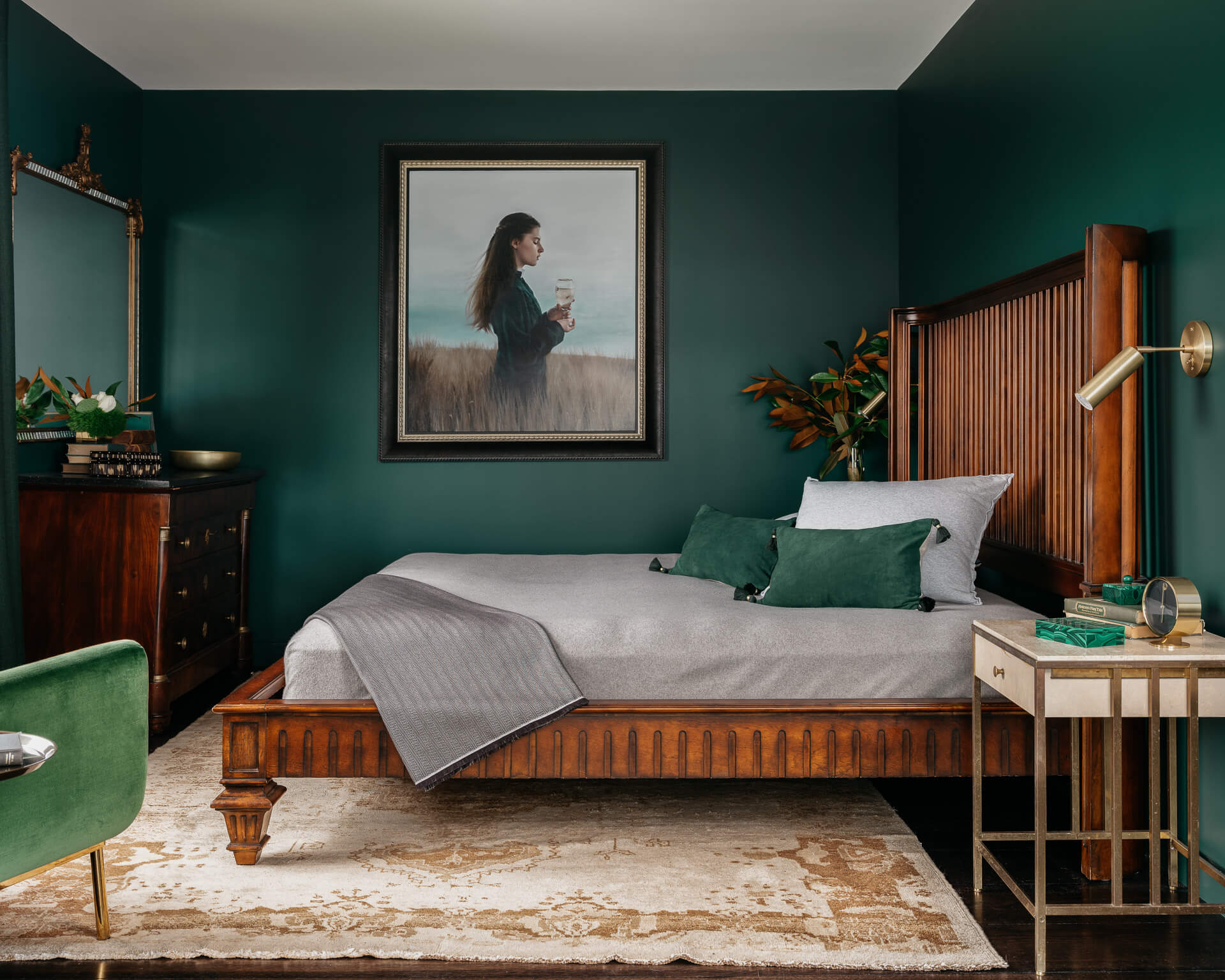 Deep green bedroom with wood bed, framed portrait, coordinating green bedding, and brass wall lights.