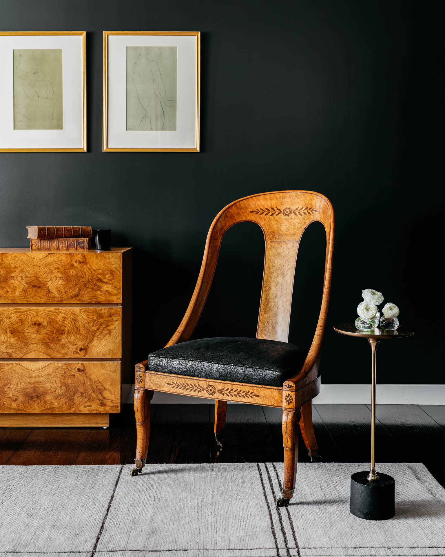Sculptural wood chair beside a burled wood chest against a deep green wall.