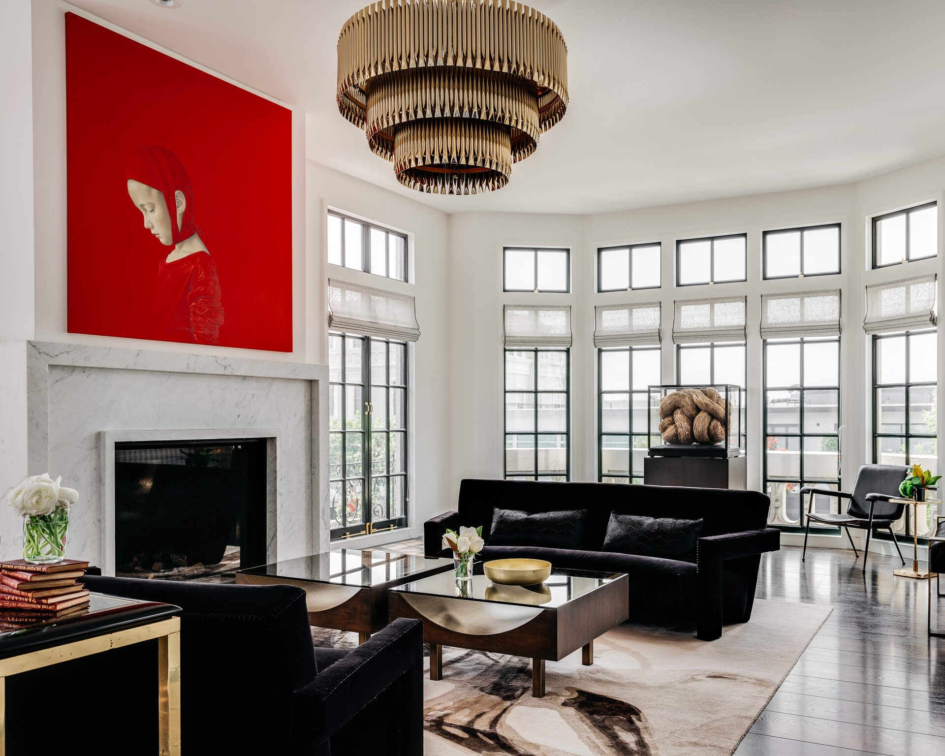 Bright living room with black seating, white fireplace, large red artwork, and wraparound windows.