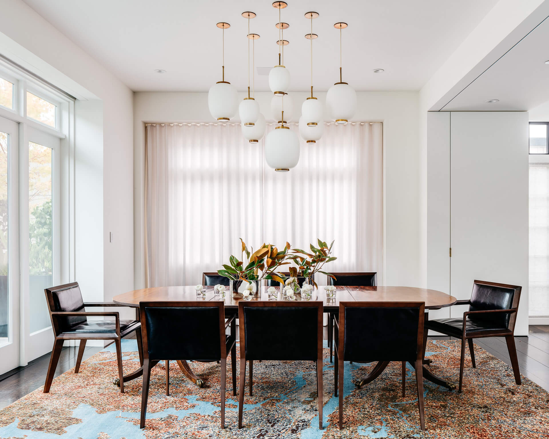 Dining room with long wood table, dark chairs, clustered pendant lights, and a patterned rug.