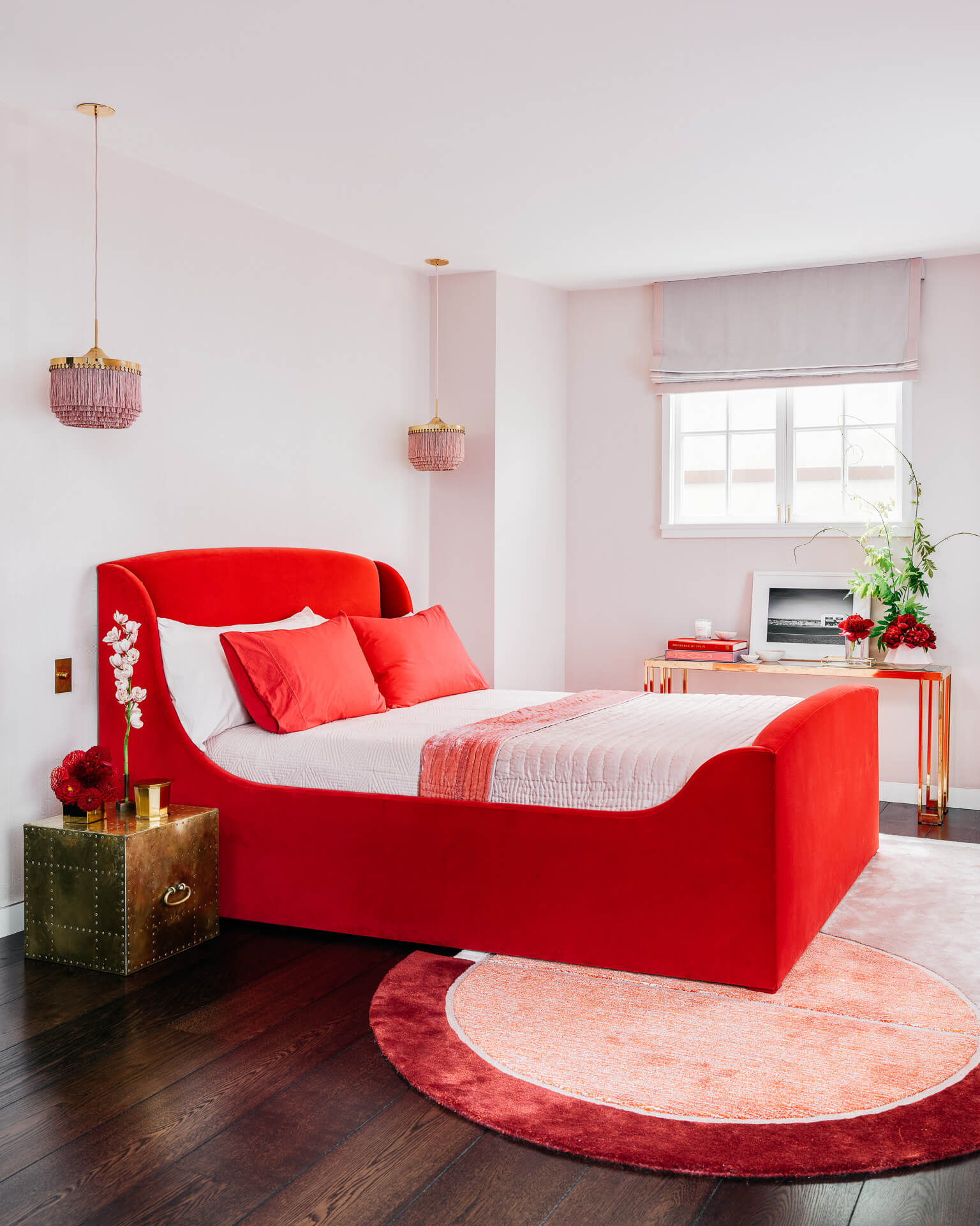 Playful bedroom with bright red bed, pink walls, pendant lights, and a round red-and-pink rug.