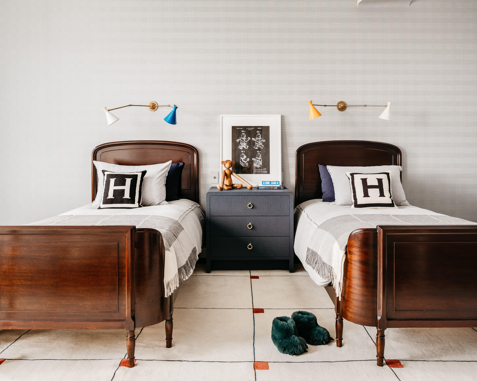 Symmetrical bedroom with twin wood beds, dark nightstand, patterned pillows, and matching wall lights.