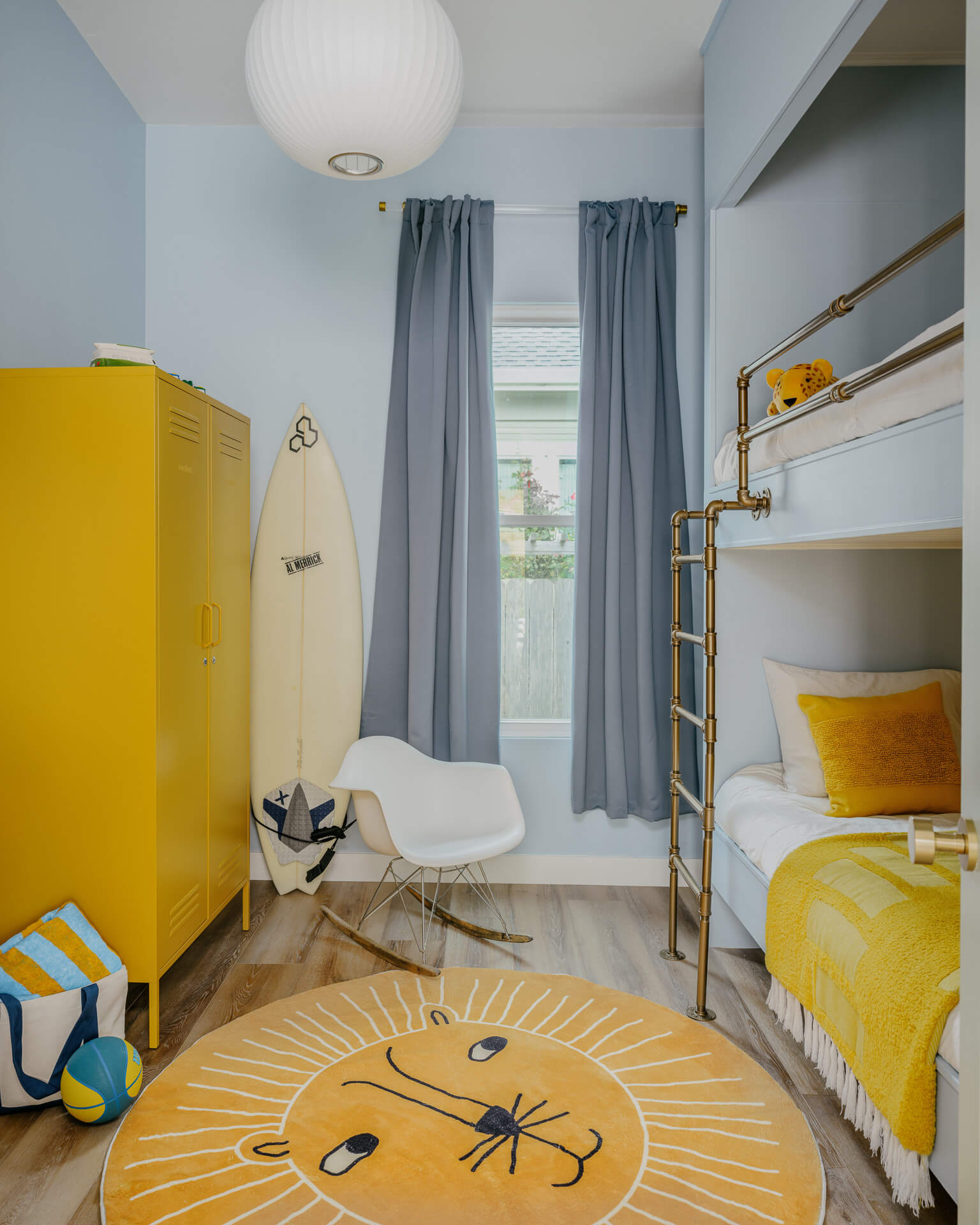 Playful children’s room with yellow locker, bunk bed, surfboard, gray curtains, and round lion rug.