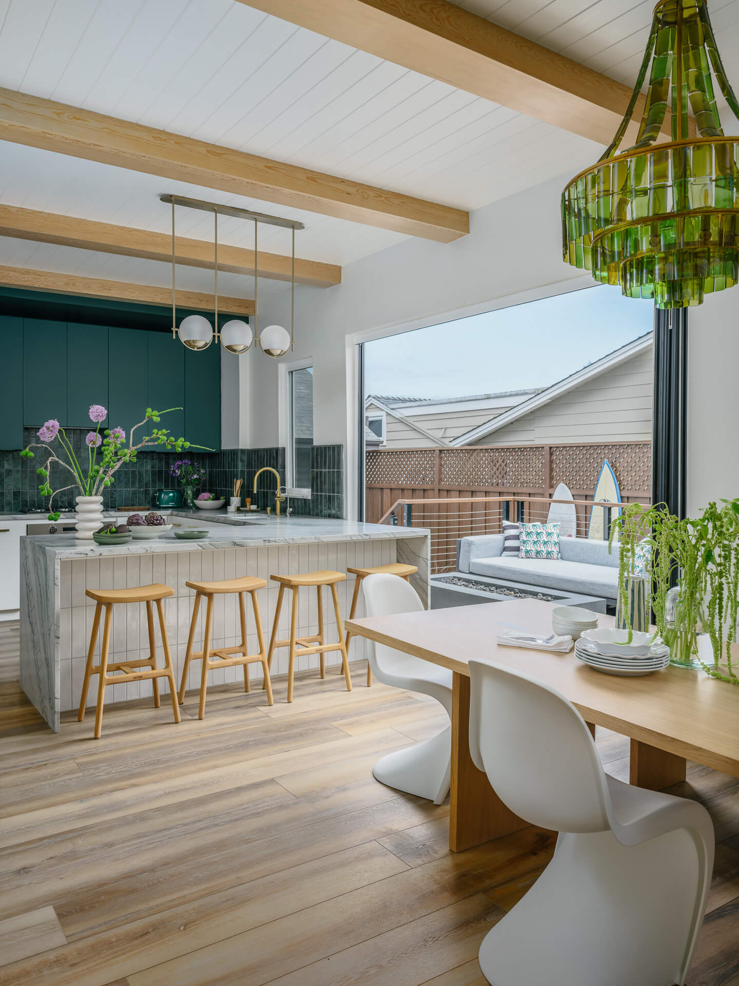 Open kitchen and dining area with exposed wood beams, white island, wood stools, green cabinetry, and large patio doors.
