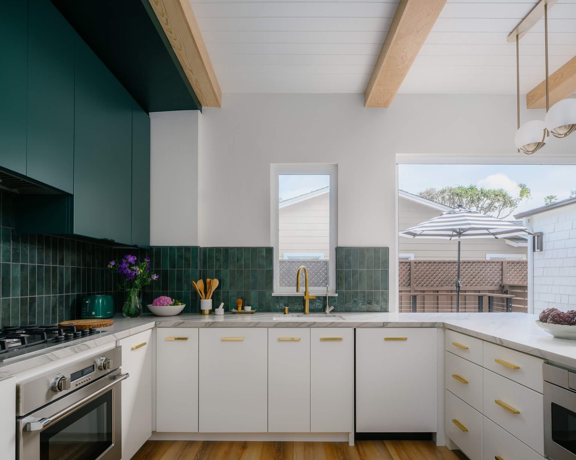 Bright kitchen with white cabinetry, deep green uppers, brass hardware, exposed beams, and wood floors.