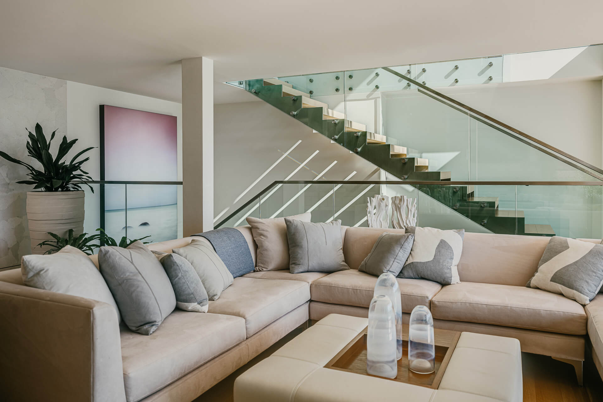 Relaxed sitting area with L-shaped sectional beneath a glass-and-metal staircase.