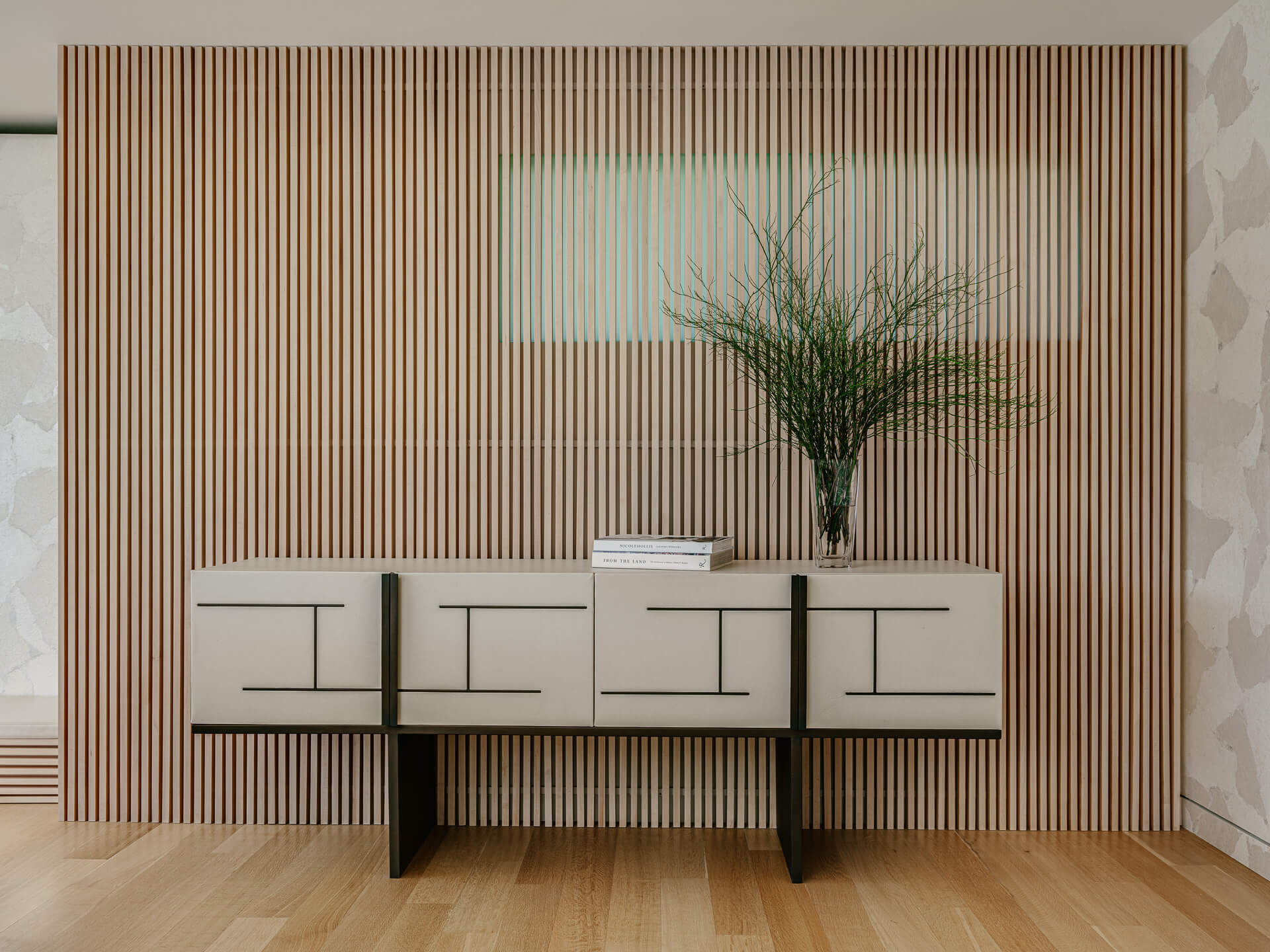 Floating white credenza against a vertical wood-slat wall with a tall vase of branches.