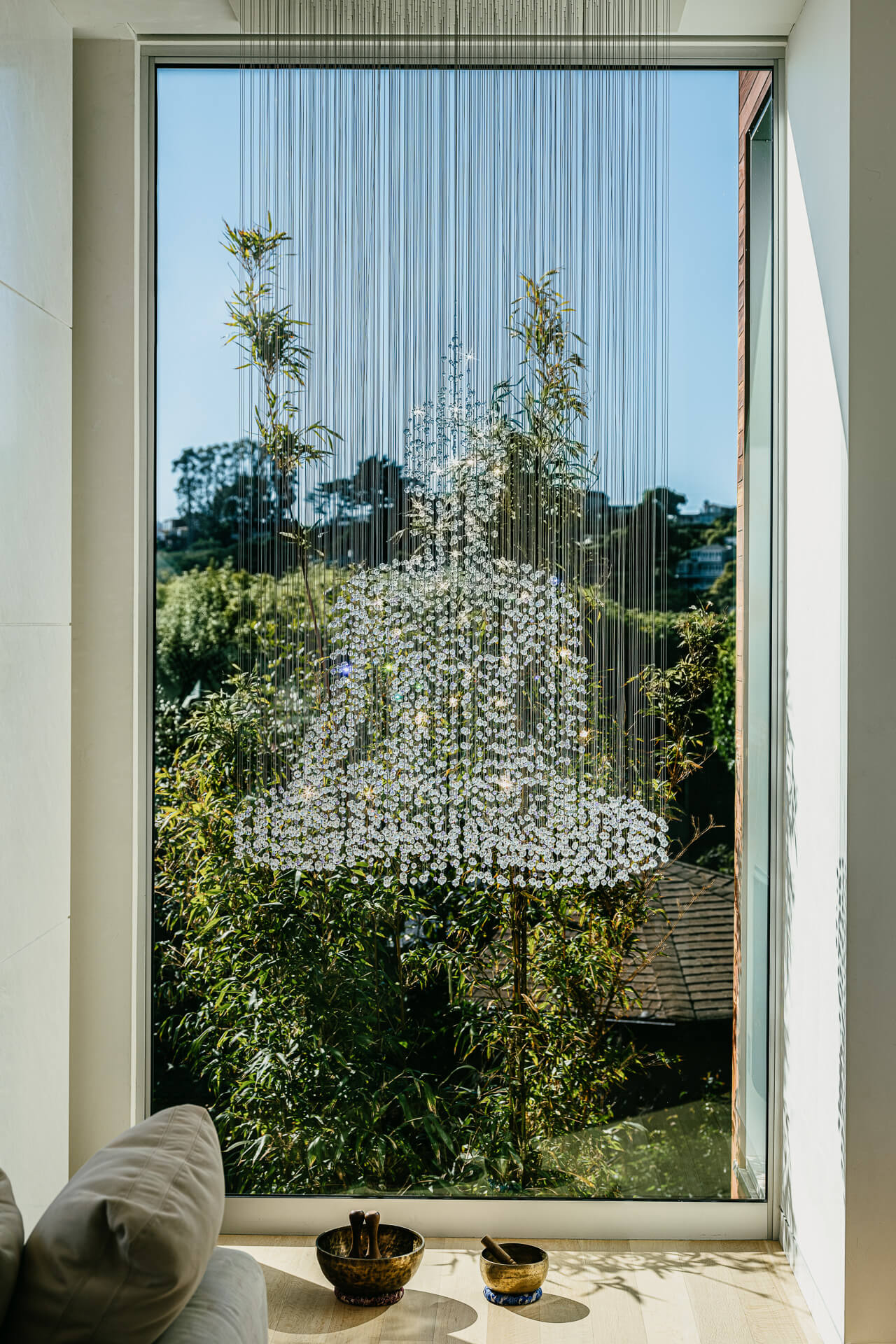 Tall window overlooking trees and water, framed by a delicate hanging installation.
