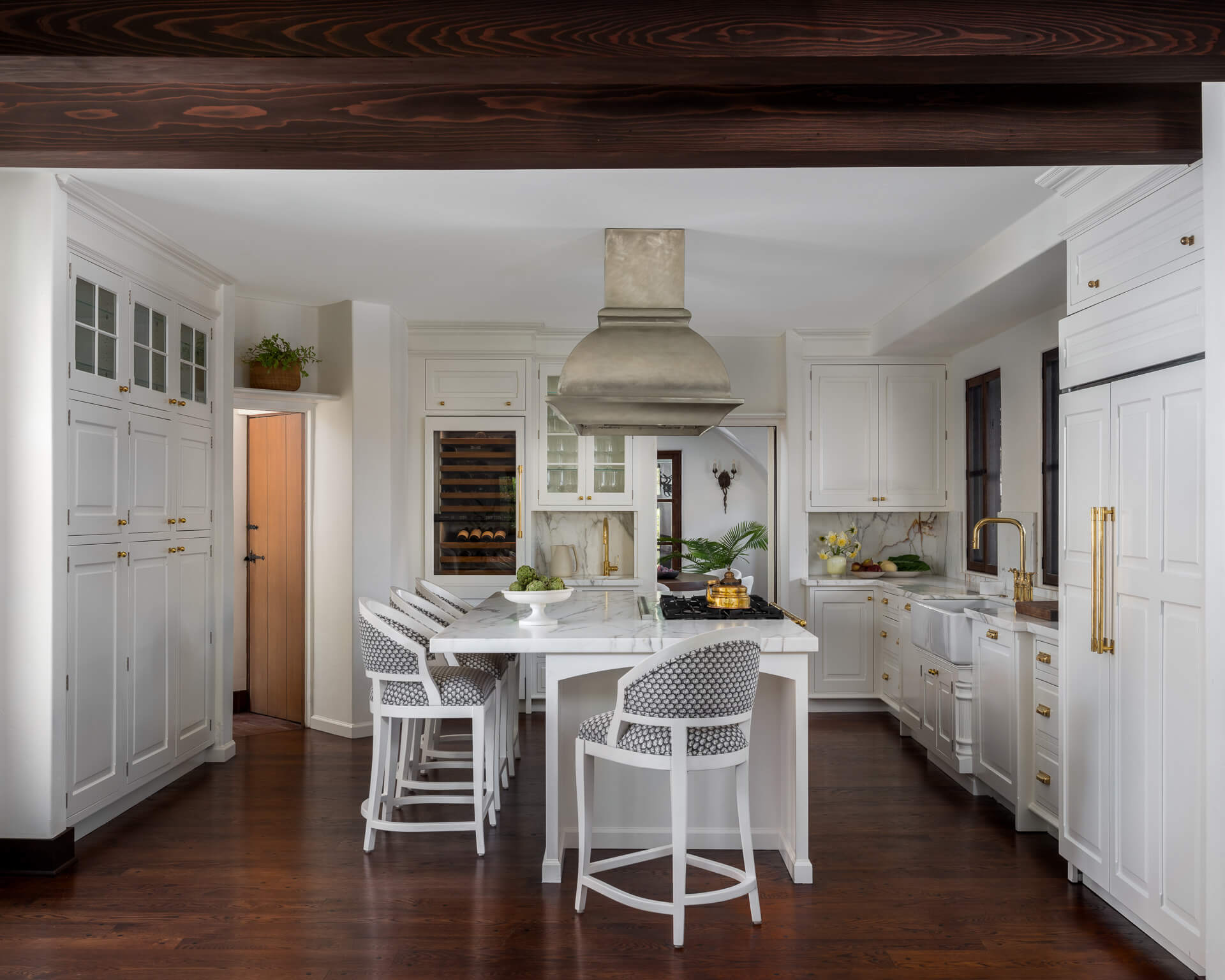 Bright white kitchen with central island, white stools, dark wood floors, and exposed ceiling beam.