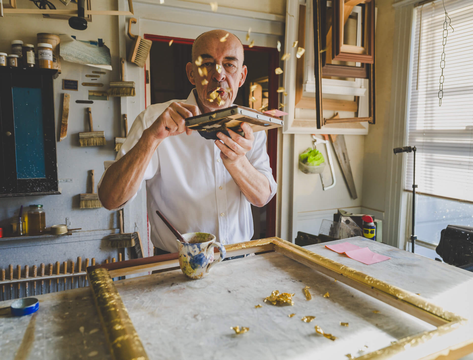 Peter Werkhoven working at a studio table surrounded by tools, shelves and warm daylight.