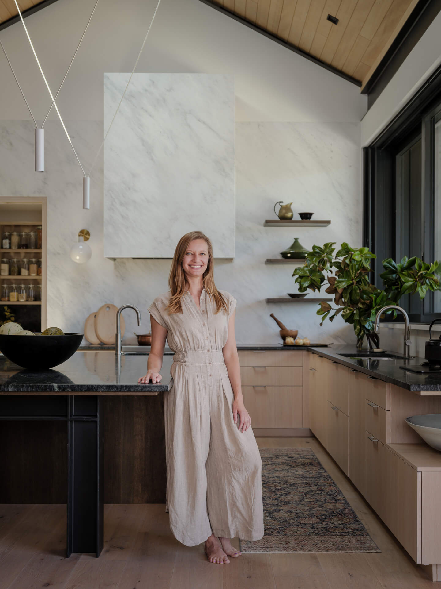 Andrea Lackie standing in a contemporary kitchen with pale cabinetry and marble surfaces.