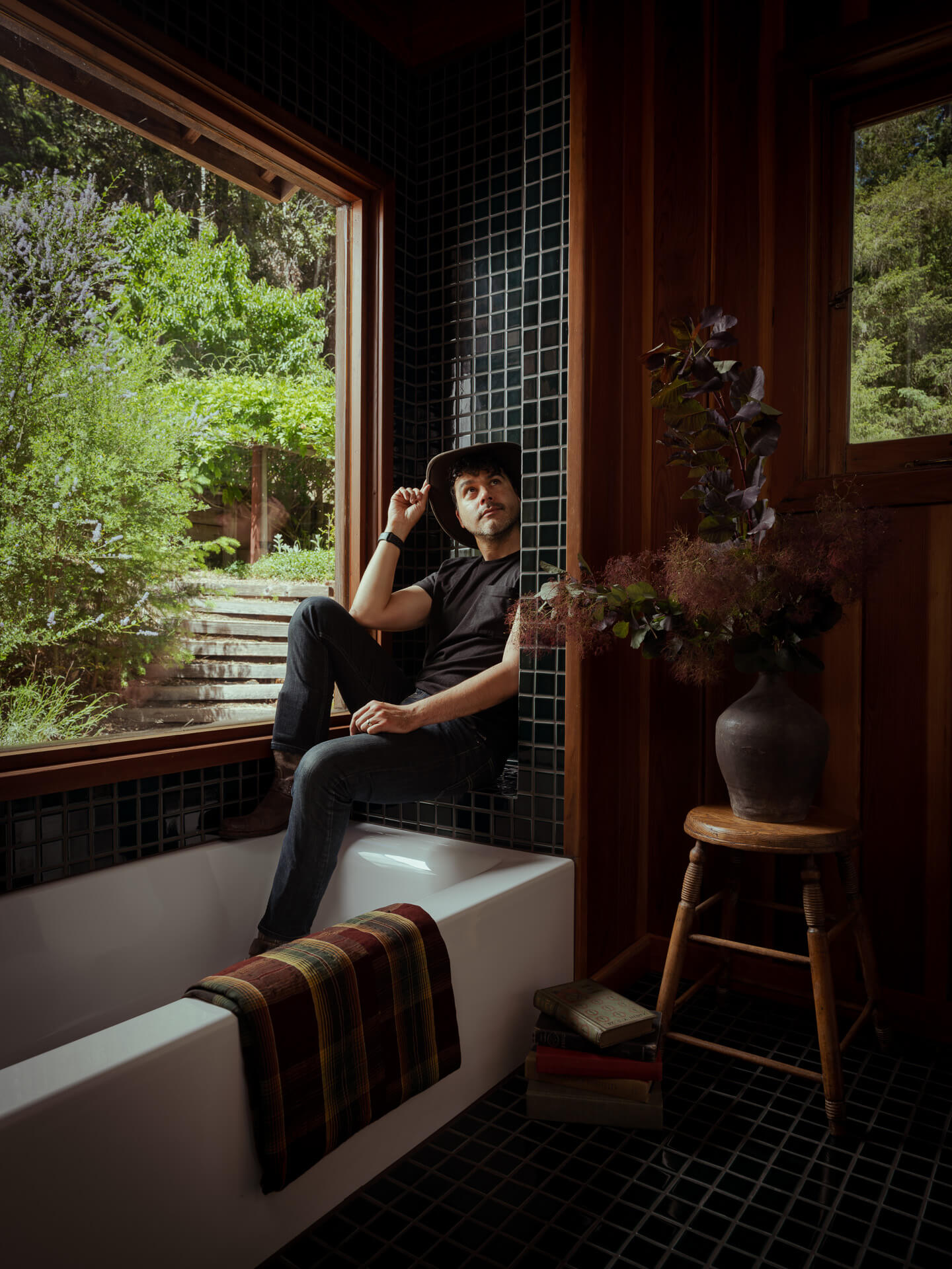 Anthony Rodriguez seated beside a window in a dark wood interior overlooking greenery.