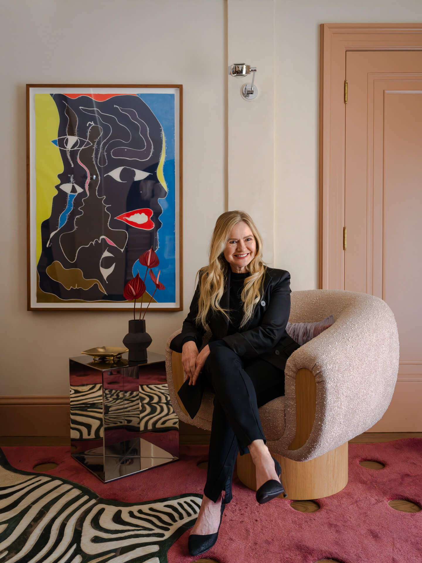 Woman seated in a sculptural pink chair beside bold artwork and a zebra-patterned rug.