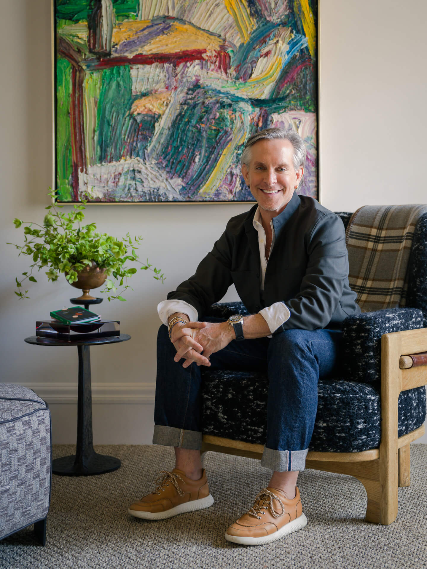 Jay Jeffers seated in a blue patterned chair with colorful abstract artwork behind him.