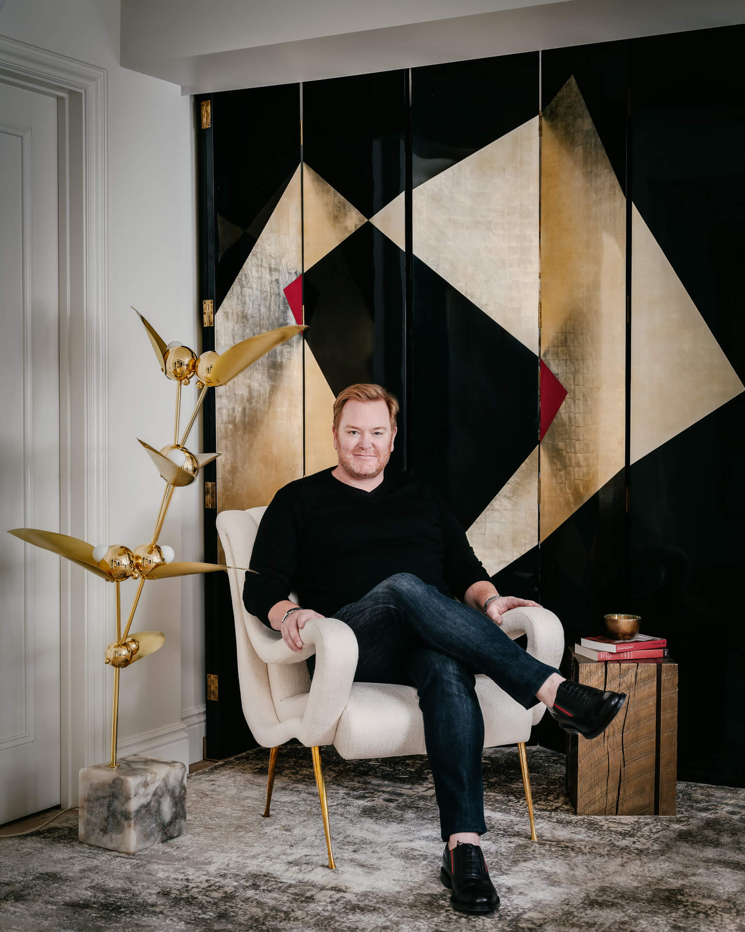 Jeffrey Neve seated in a white chair in front of bold black-and-gold geometric artwork.