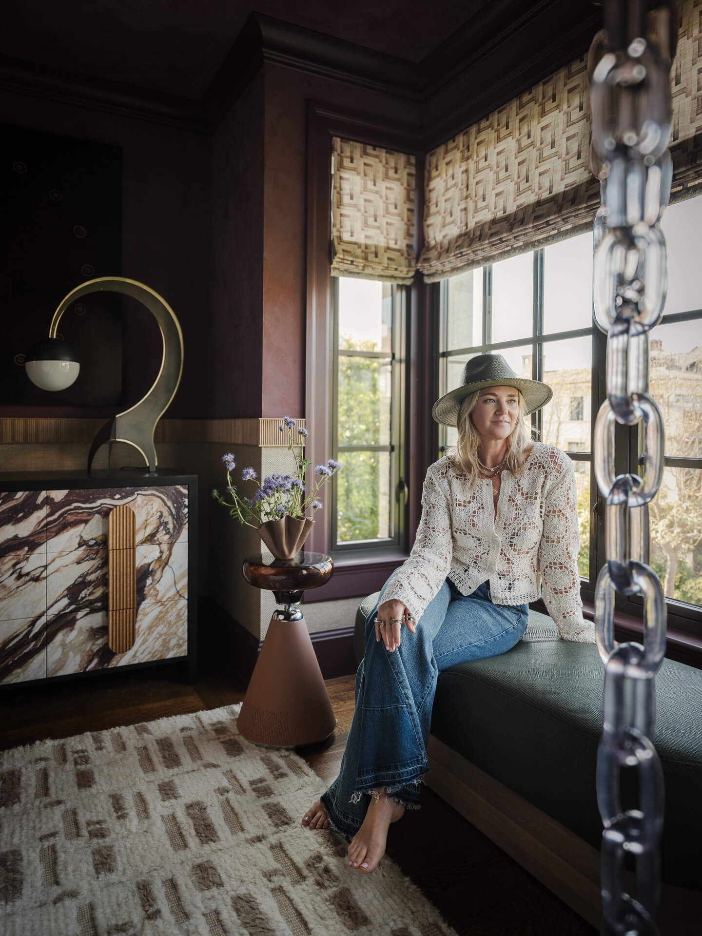 Kendra Nash seated in a layered interior with dark wood, patterned textiles and sculptural metalwork.